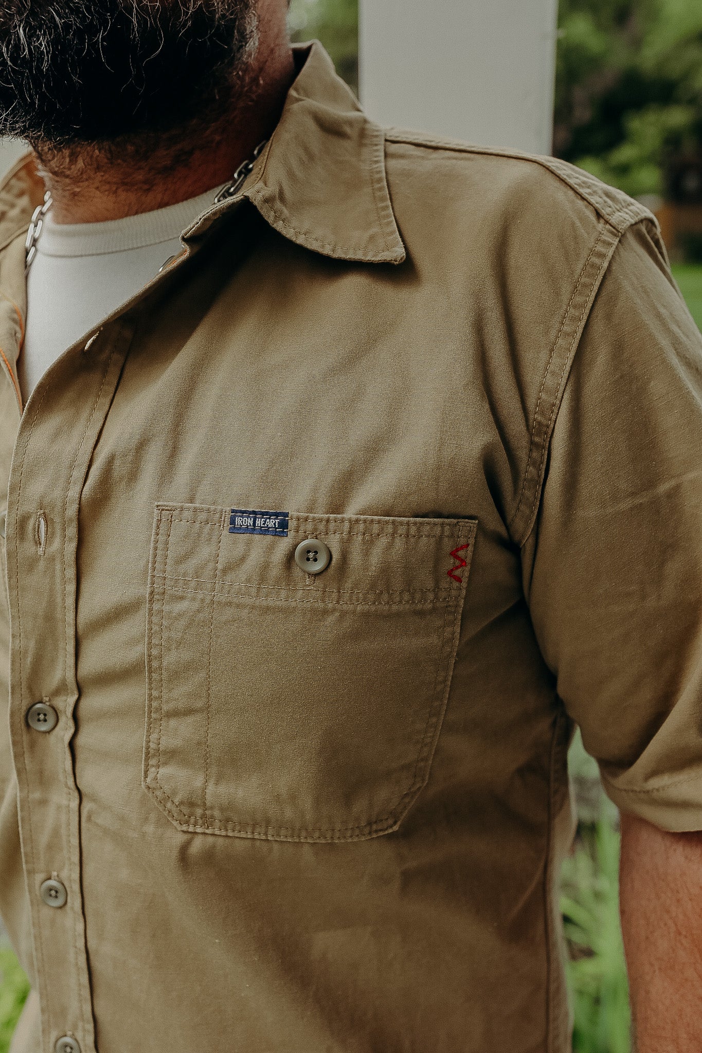 Close-up of man wearing tan Iron Heart short-sleeve button shirt with front pocket outdoors