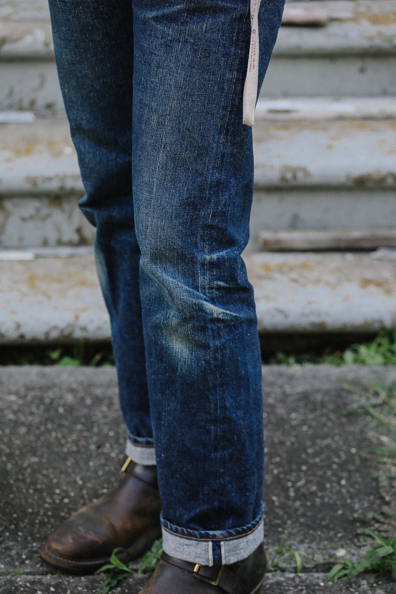 Close-up of worn blue jeans with rolled cuffs and brown leather boots on outdoor concrete steps