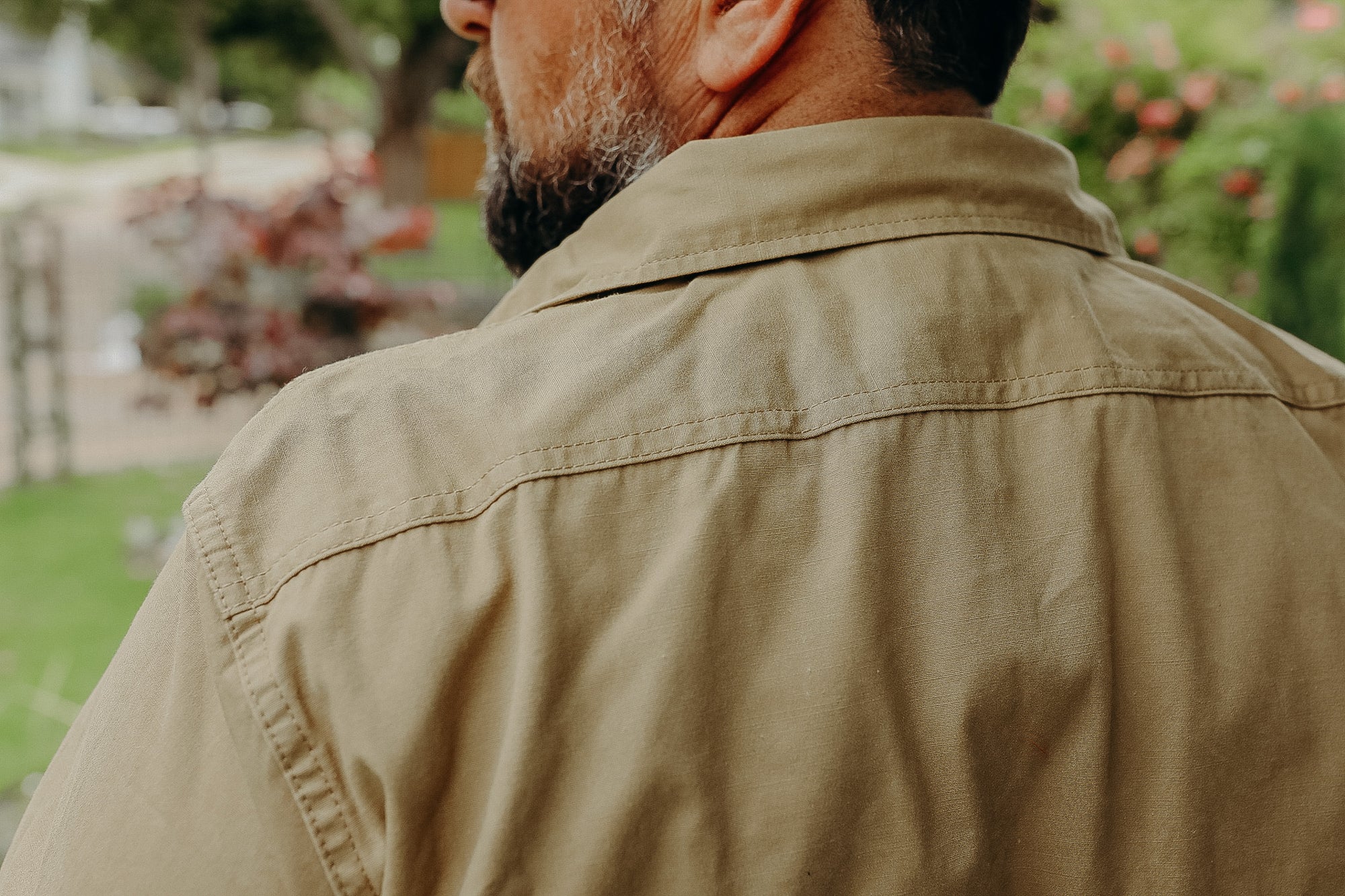 Close-up of man's shoulder and collar wearing a tan work shirt outdoors with blurred garden background