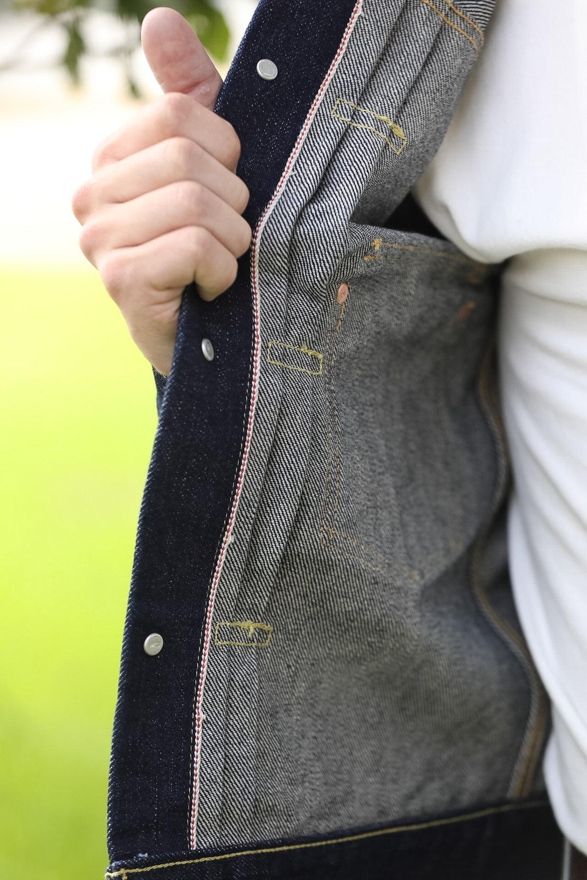 Close-up of a person holding open a dark indigo denim jacket to show the textured gray and navy woven fabric lining and contrast stitching.
