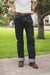A person standing outdoors on a sidewalk wearing dark indigo denim jeans with a brown belt and brown shoes, with a white t-shirt partially visible.