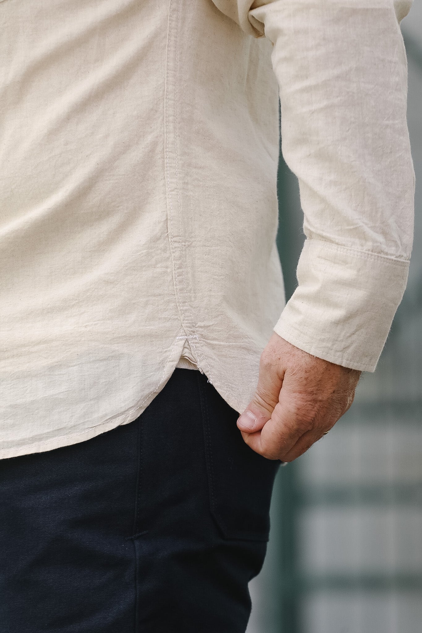 Person wearing a beige long-sleeve shirt and dark pants against a blurred background