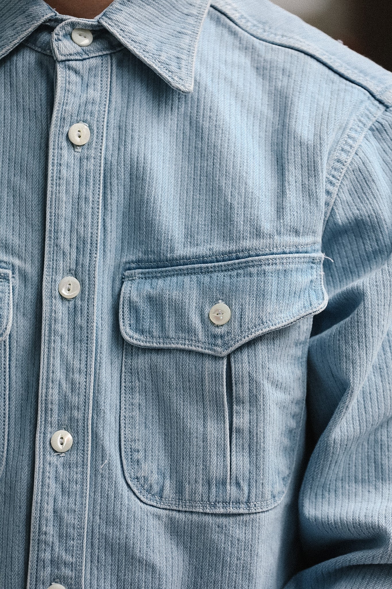 Close-up of a light blue denim shirt with buttons and a pocket.