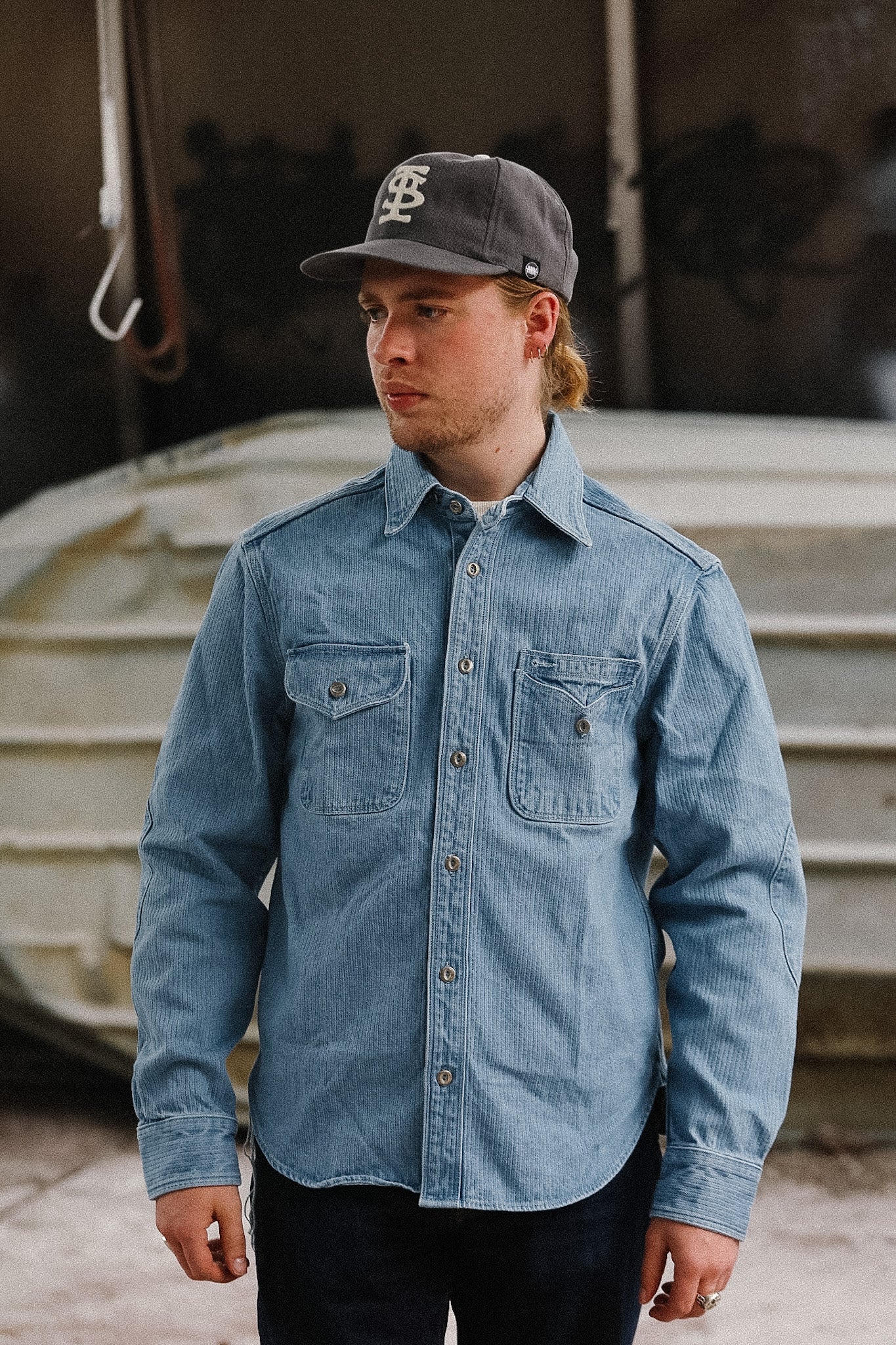 Man wearing a blue denim shirt and gray cap standing in front of a boat.
