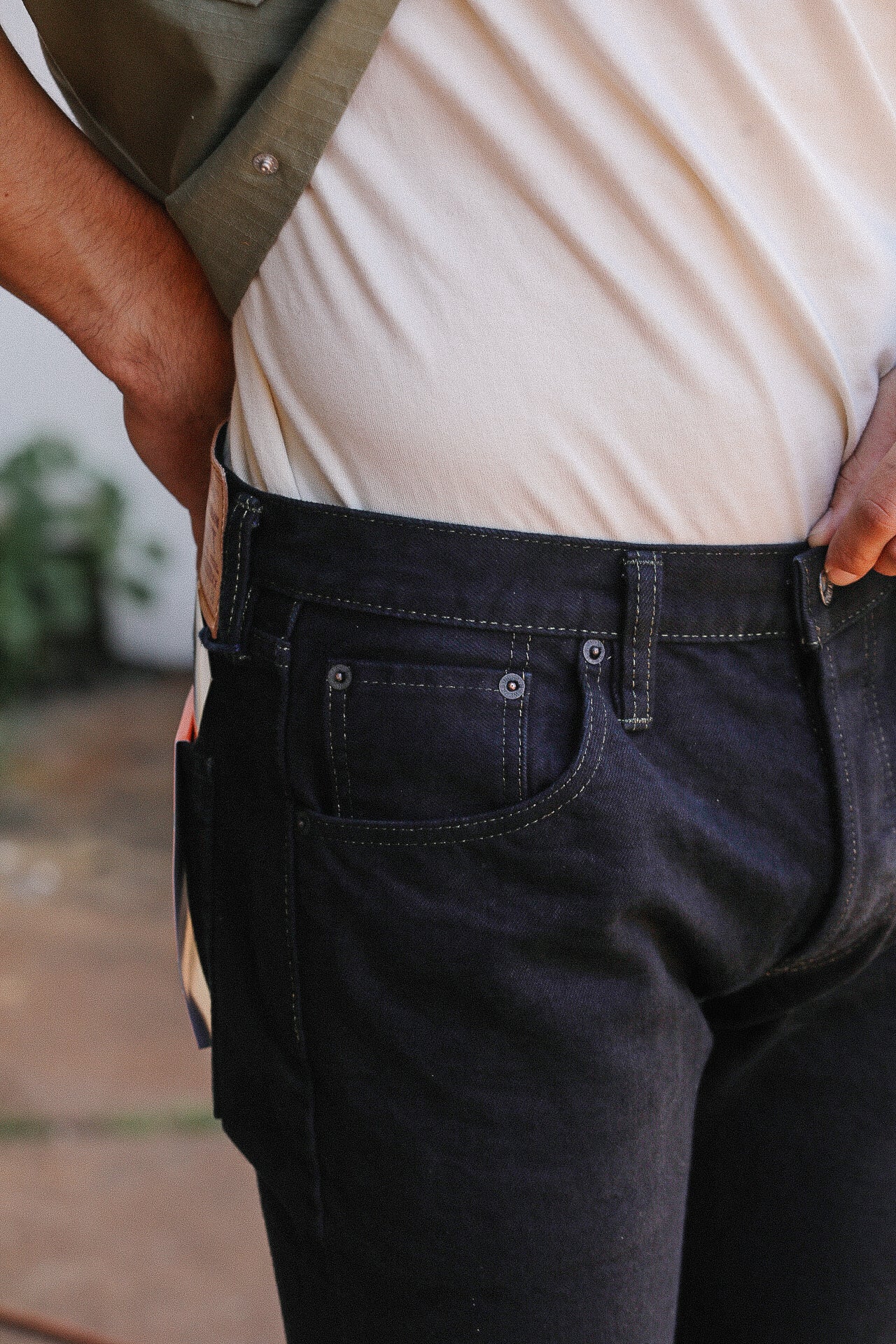 Close-up of person wearing black denim jeans with visible stitching and white shirt tucked in