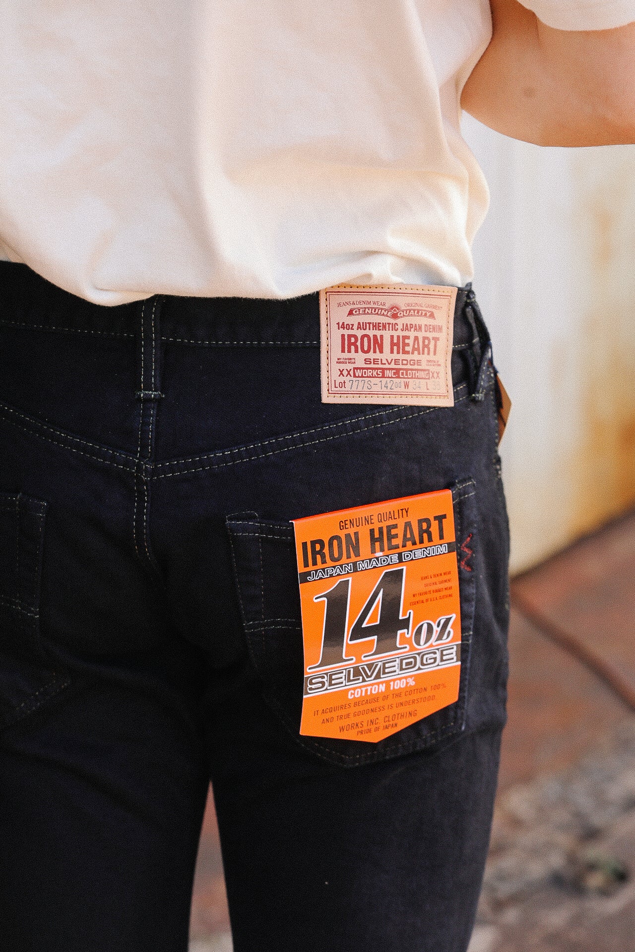 Close-up of person wearing black Iron Heart 14oz selvedge denim jeans with visible leather patch and orange tag