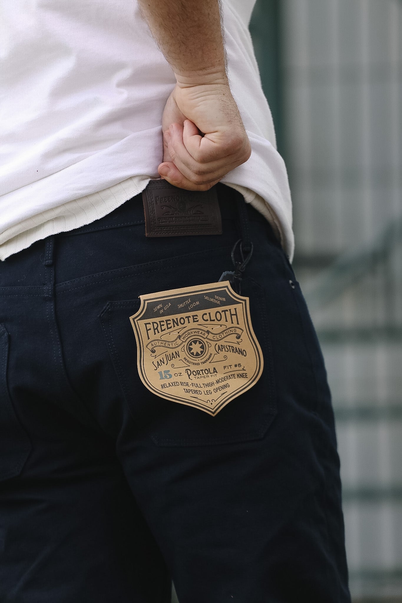 Close-up of dark pants with a brand label on the pocket against a blurred background