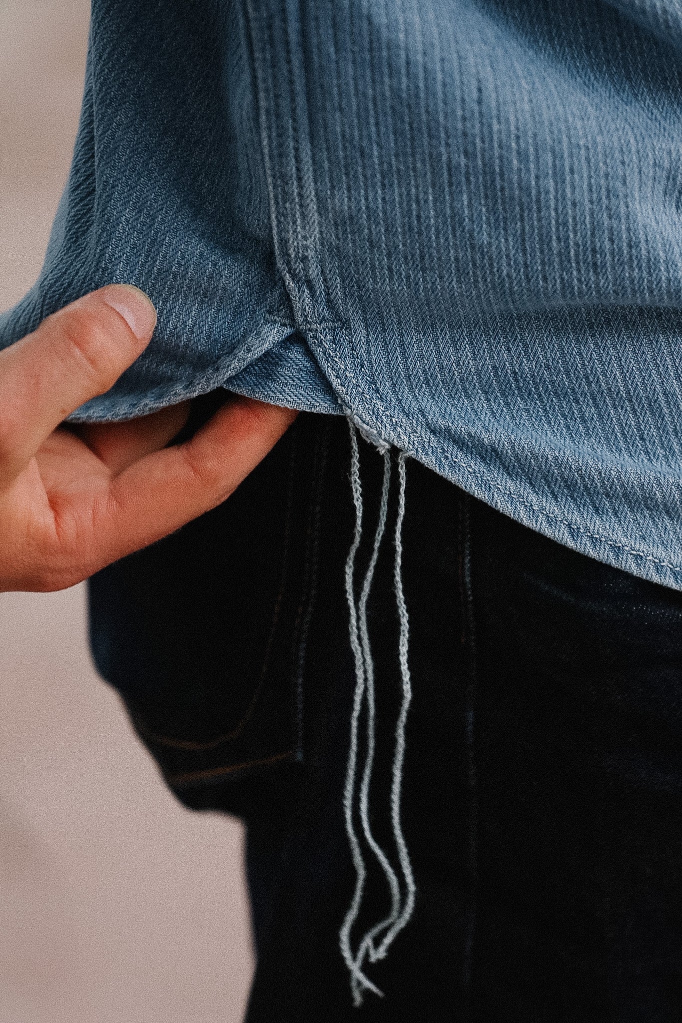Close-up of a hand adjusting a blue denim shirt with black pants.