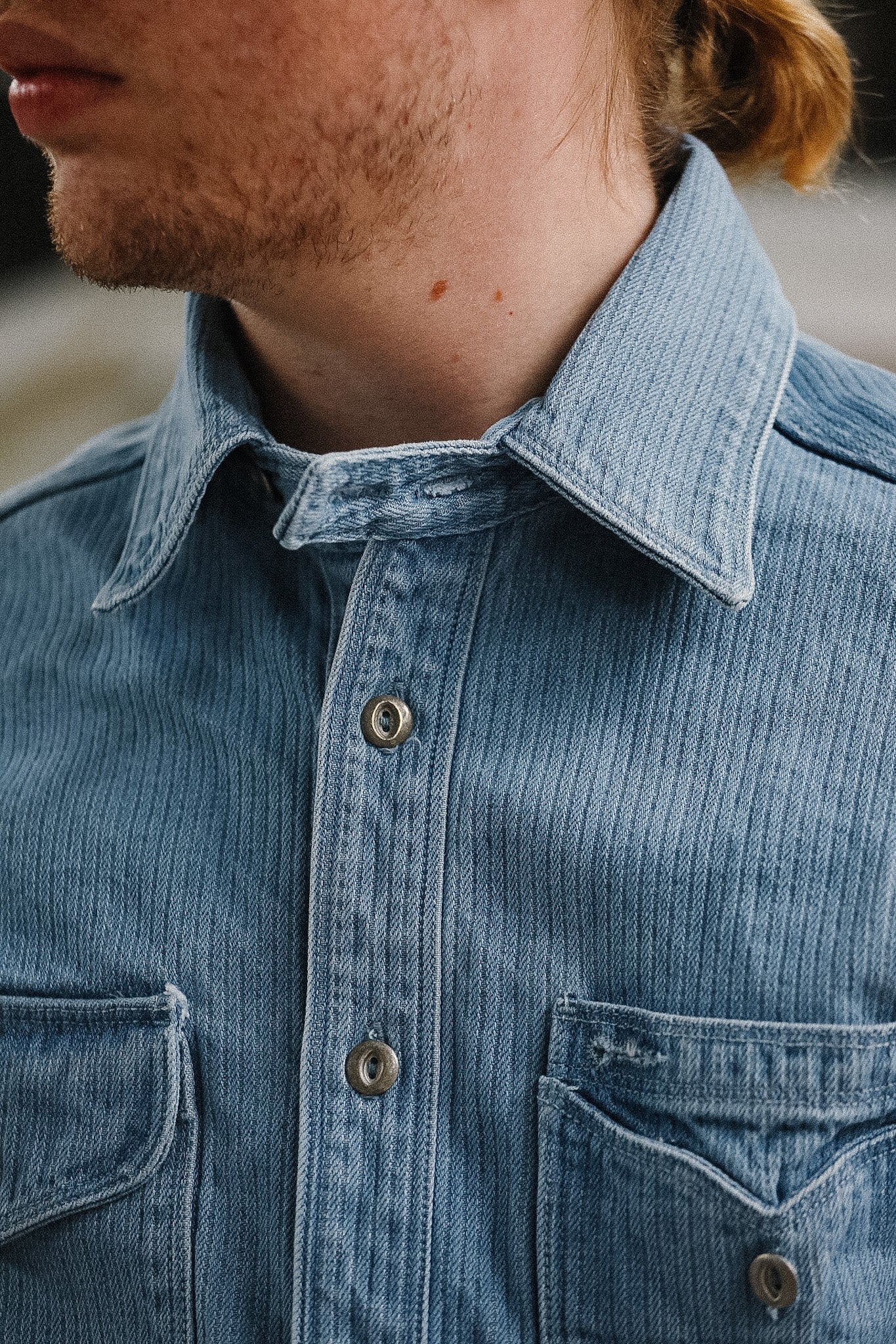 Close-up of a person wearing a blue denim shirt with a blurred background