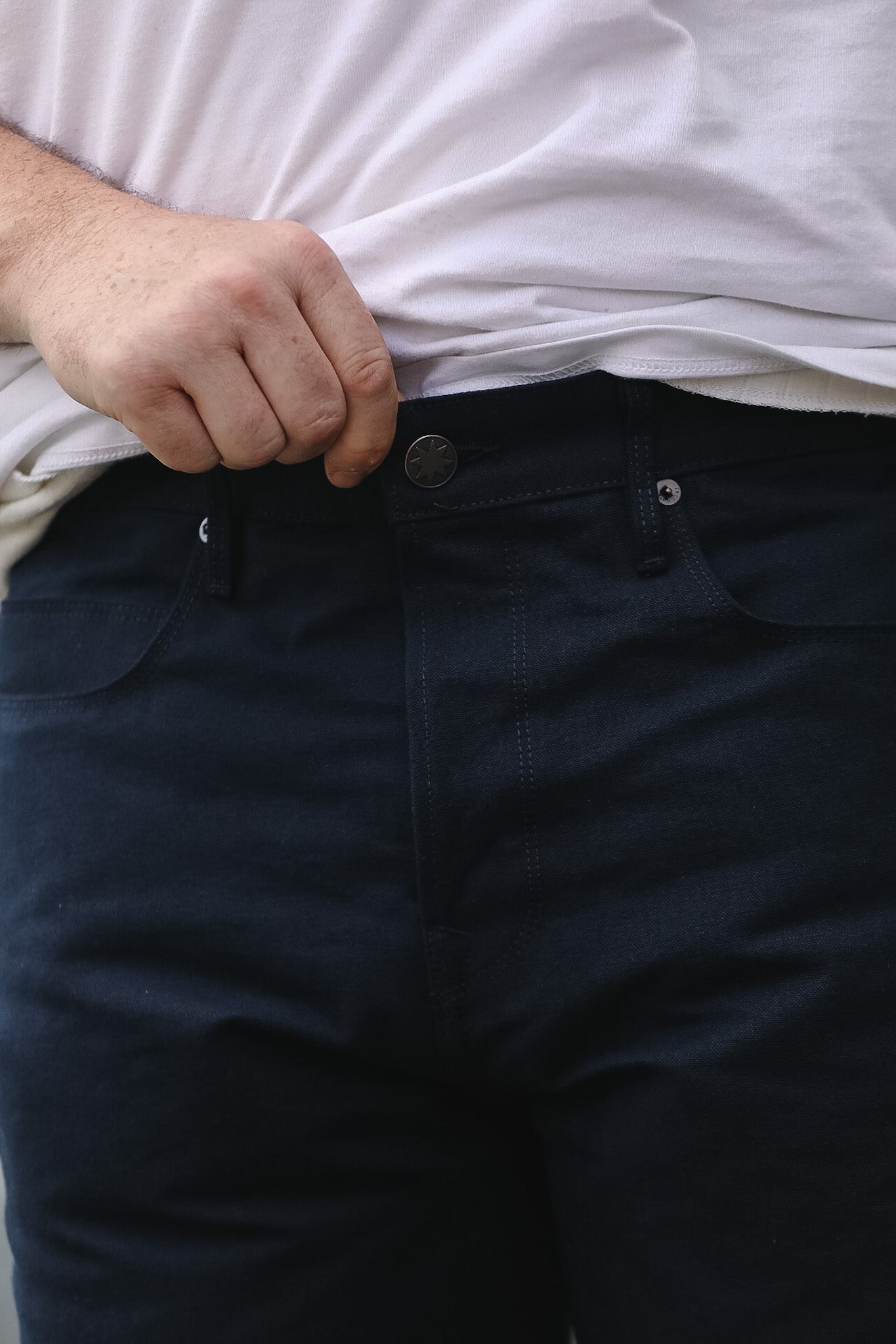 Person wearing dark blue pants and a white shirt, focusing on the waist area.