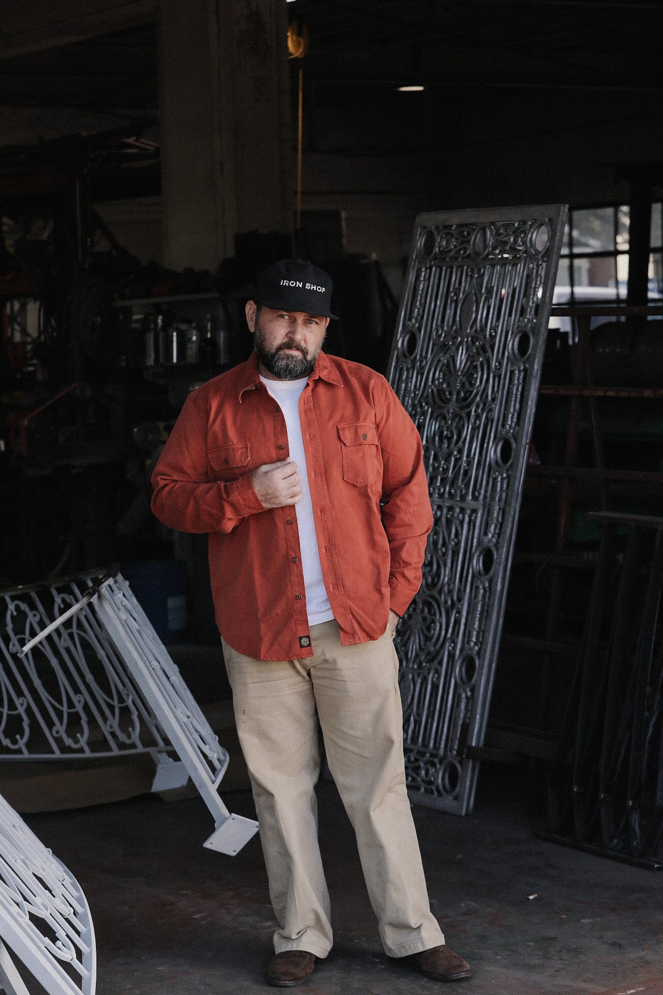 Man wearing Iron Shop hat and rust shirt standing in workshop with decorative iron gates