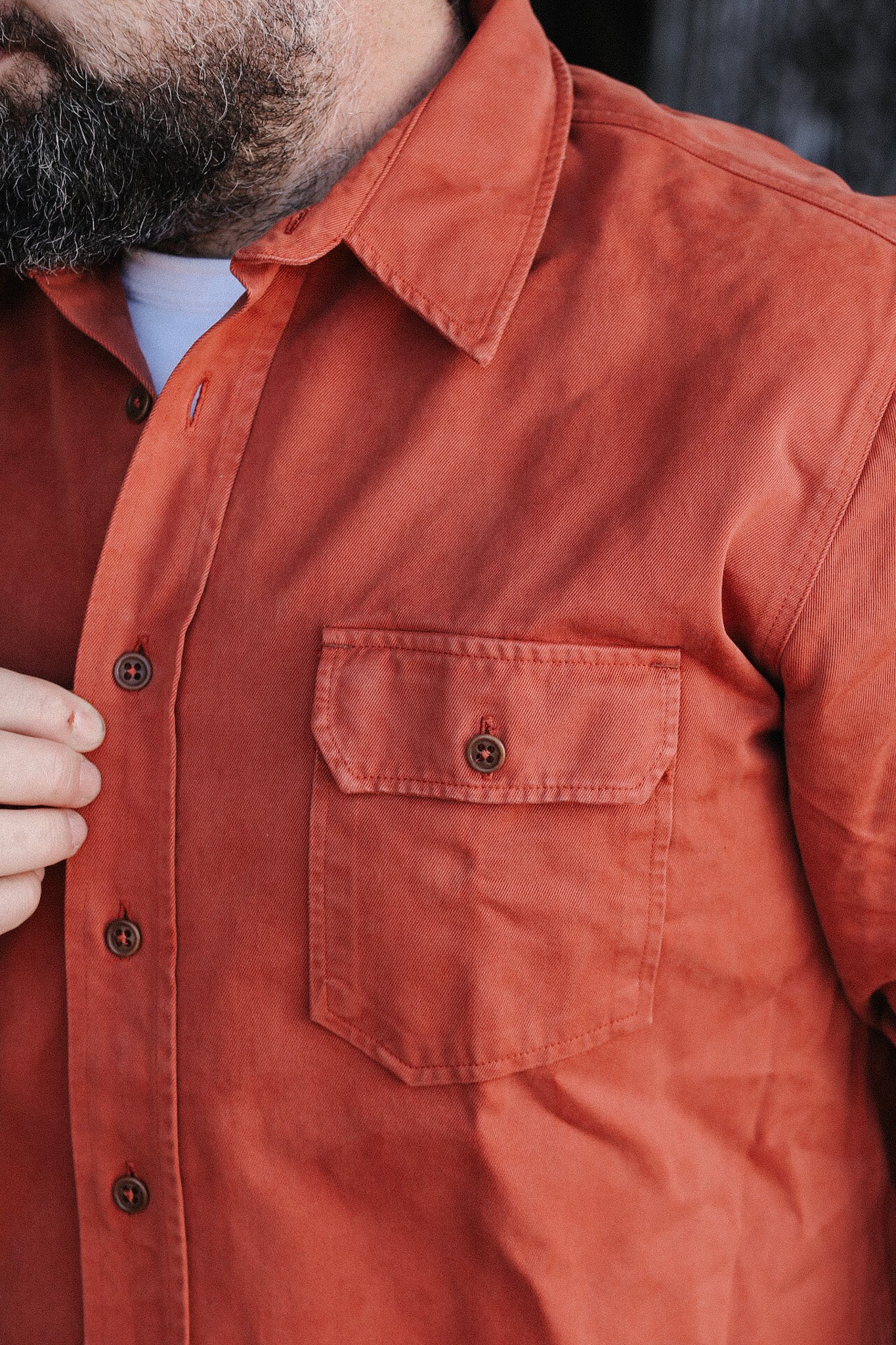 Close-up of man wearing rust orange button-up shirt with chest pocket, styled with beard and white undershirt