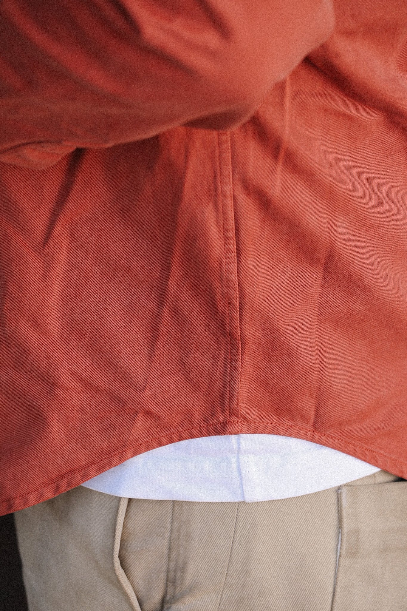 Close-up of layered clothing with rust orange shirt, white undershirt, and beige pants from Iron Shop Provisions