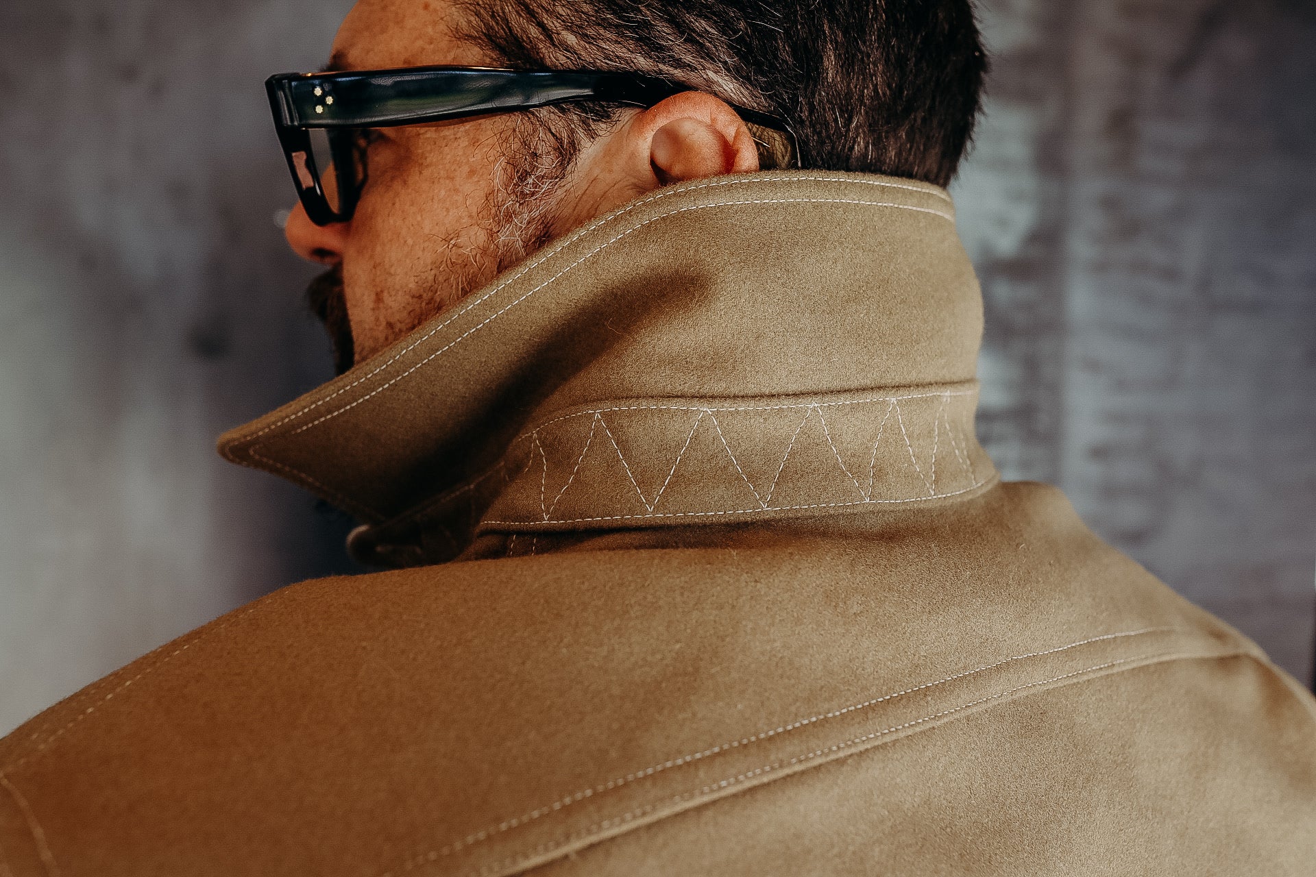Close-up of man wearing tan rugged work jacket with high collar and black glasses