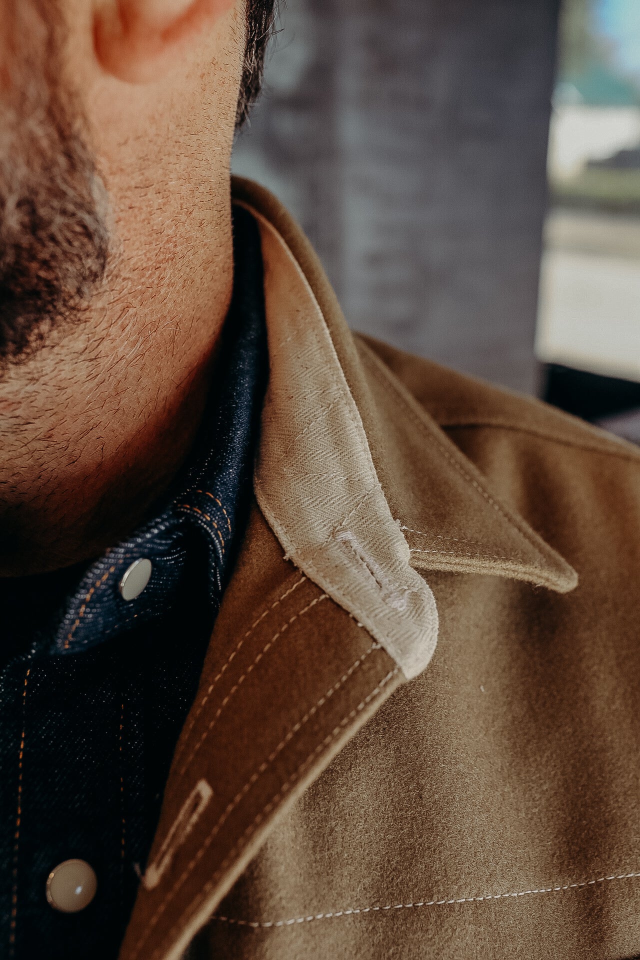 Close-up of a man wearing a brown canvas jacket with a beige collar over a dark denim shirt with metal snap buttons