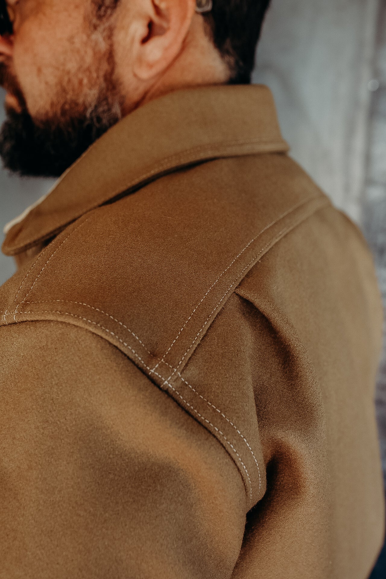 Close-up of man's shoulder wearing a camel-colored wool coat with detailed stitching