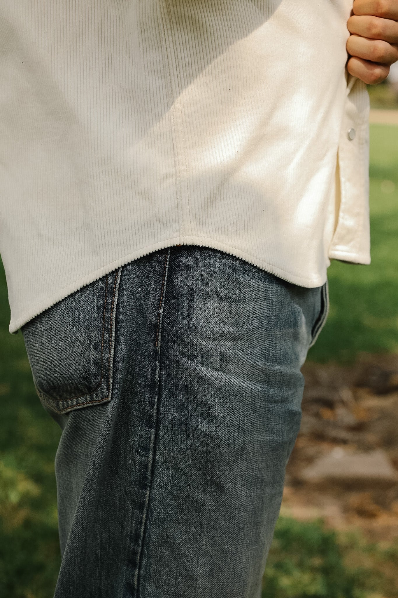 Person wearing a beige sweater and blue jeans with a blurred natural background