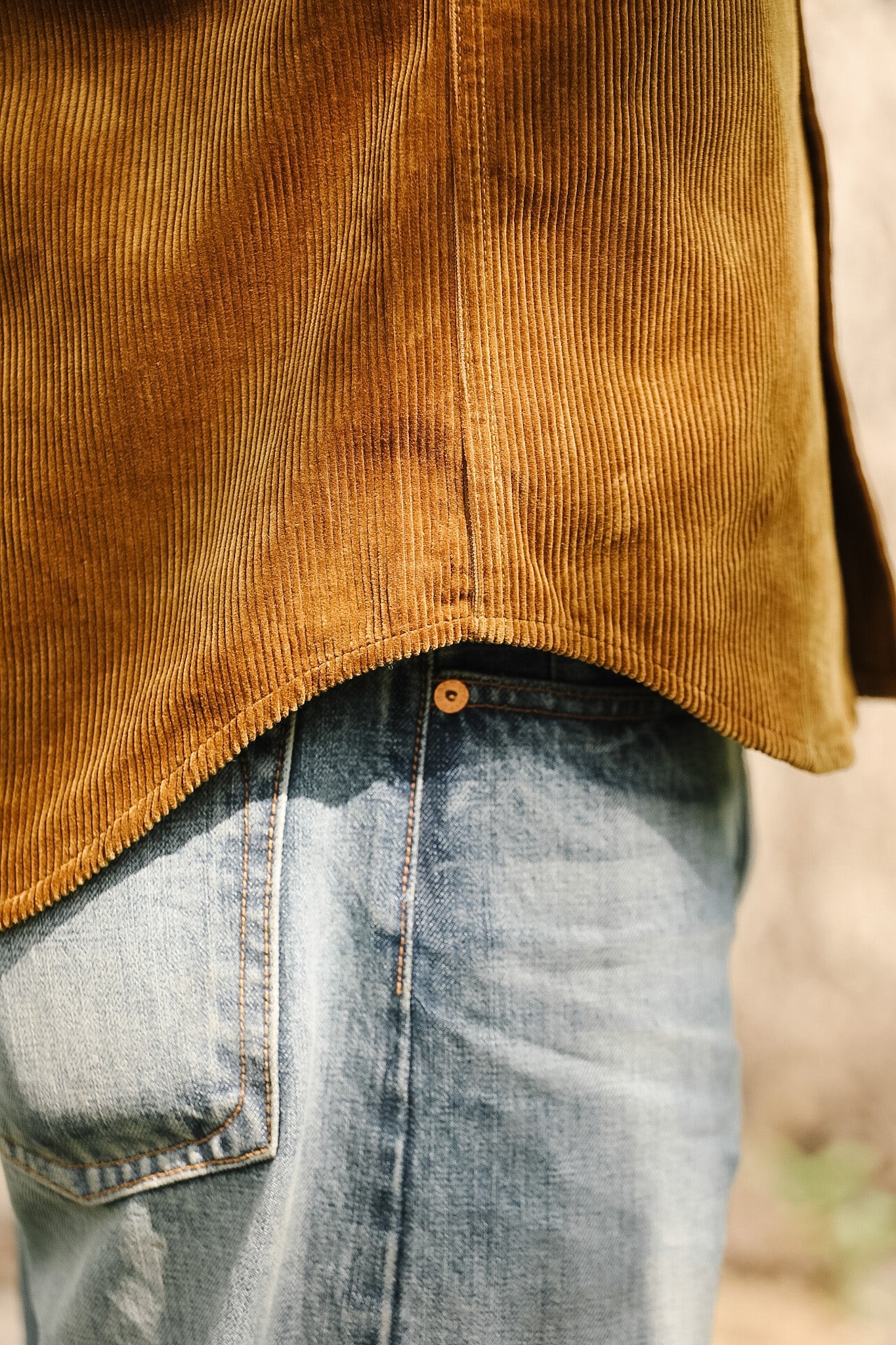 Close-up of a brown corduroy shirt and blue jeans with a blurred background
