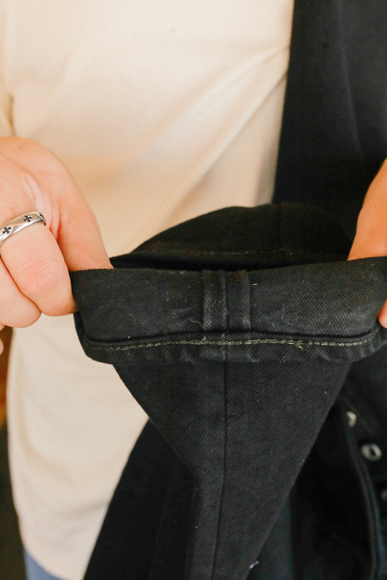 Close-up of hands holding black denim jeans cuff with visible stitching and metal ring on finger
