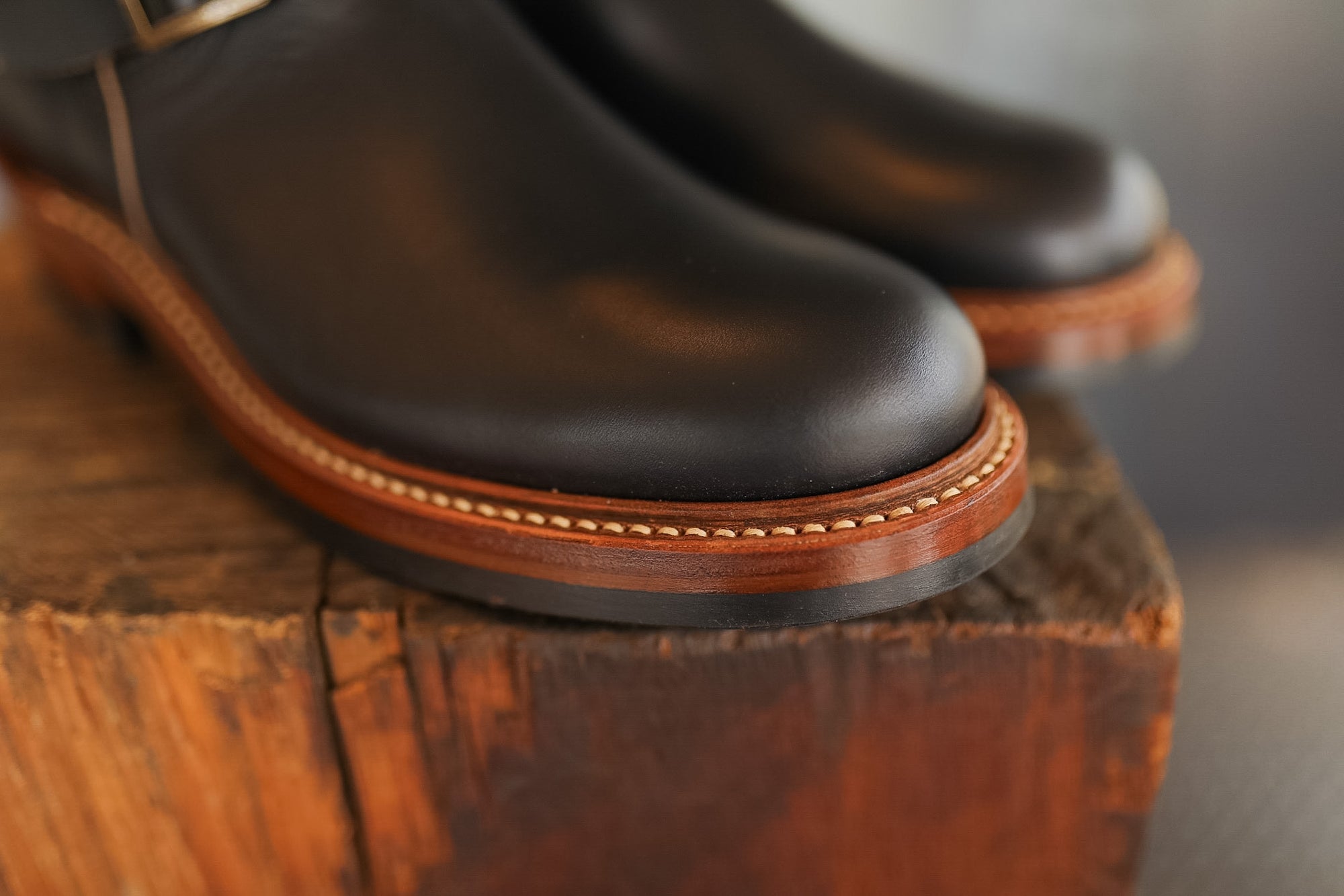 Pair of black leather boots with brown soles on a wooden surface