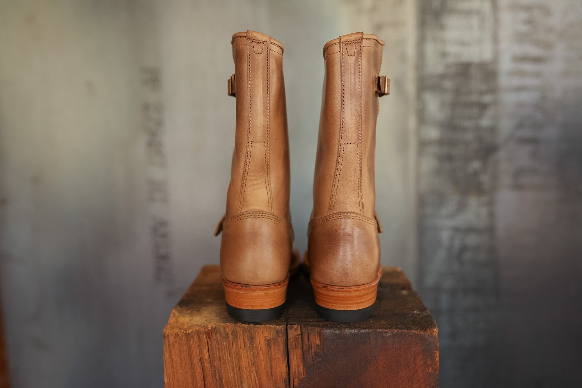 Pair of brown leather boots on a wooden block with a textured gray background