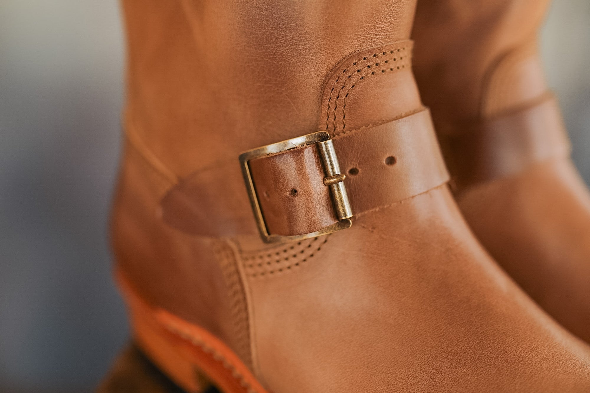 Close-up of a brown leather boot with a gold buckle on a blurred background