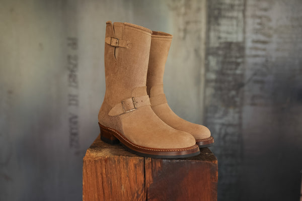 Pair of tan boots on a wooden block with a textured wall background