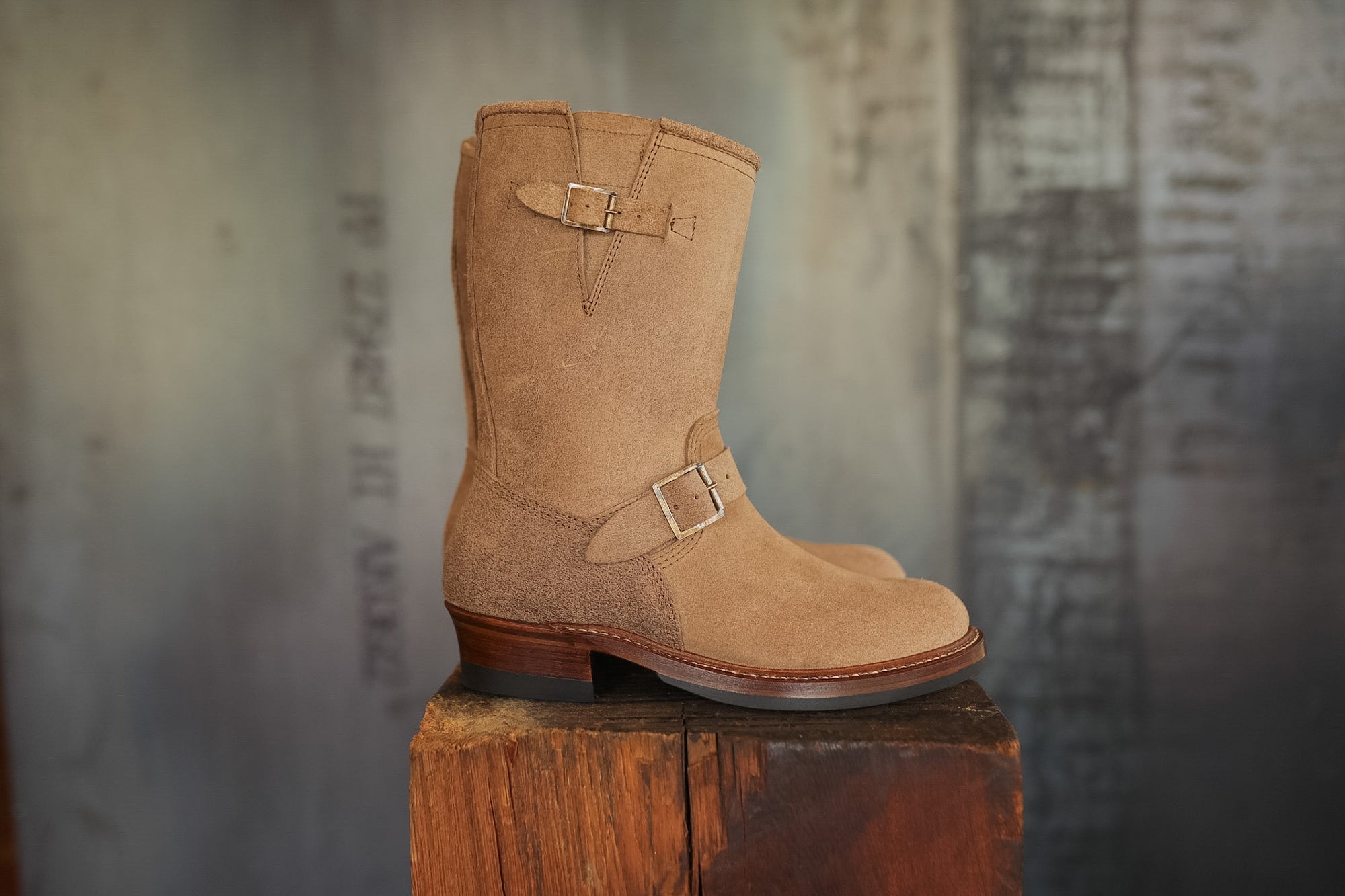Tan boot with a buckle on a wooden block against a textured gray background