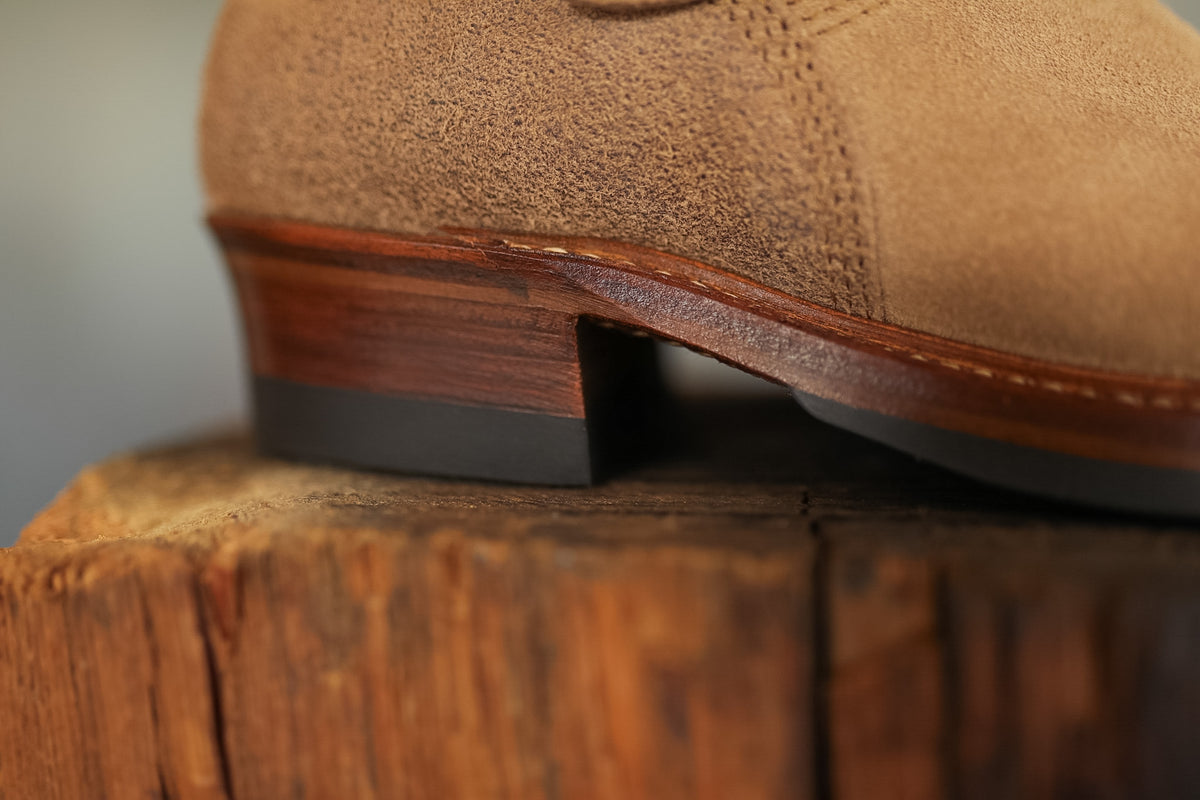 Brown suede shoe on a wooden block with a neutral background