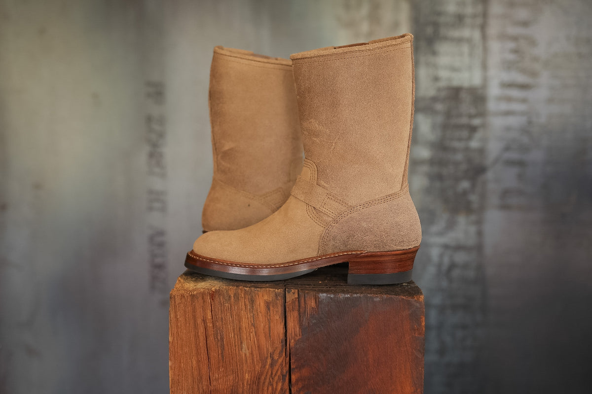 Pair of tan boots on a wooden block with a textured gray background