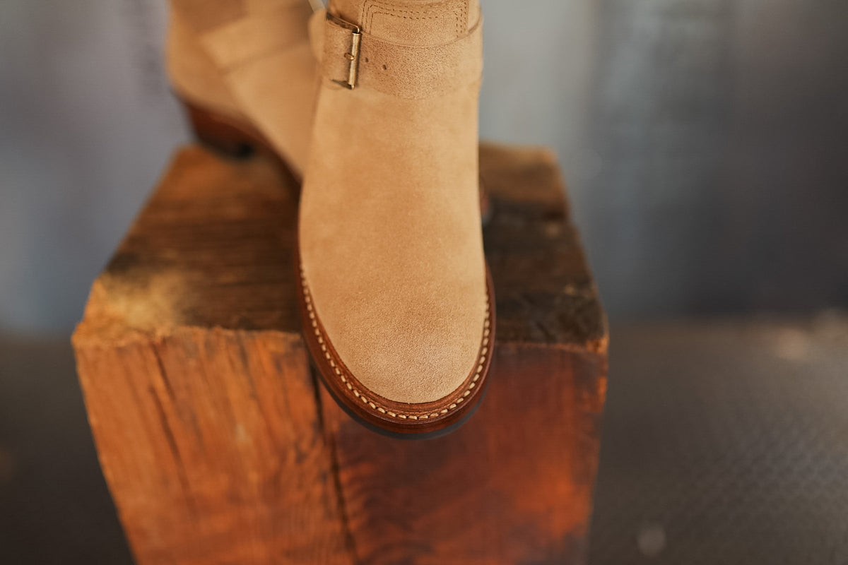 Tan suede boot on a wooden block with a blurred background