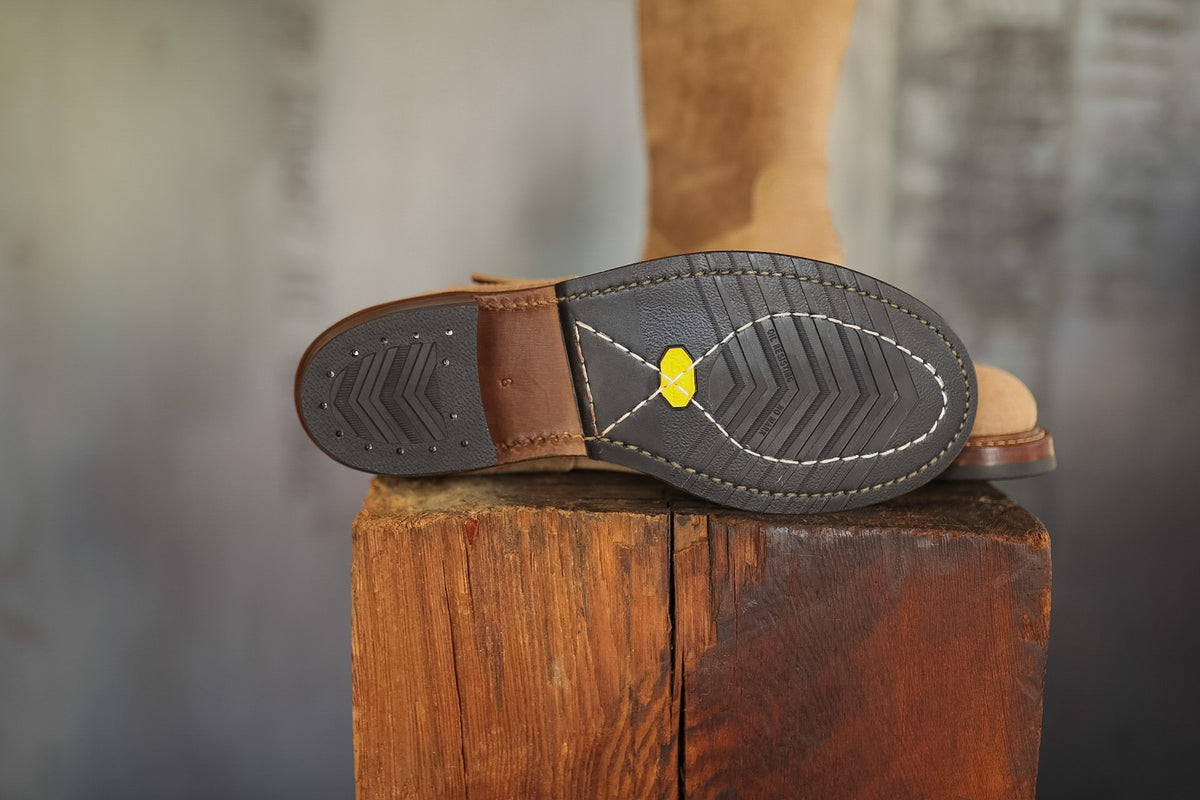 Close-up of a brown boot sole with a visible brand logo on a wooden block.