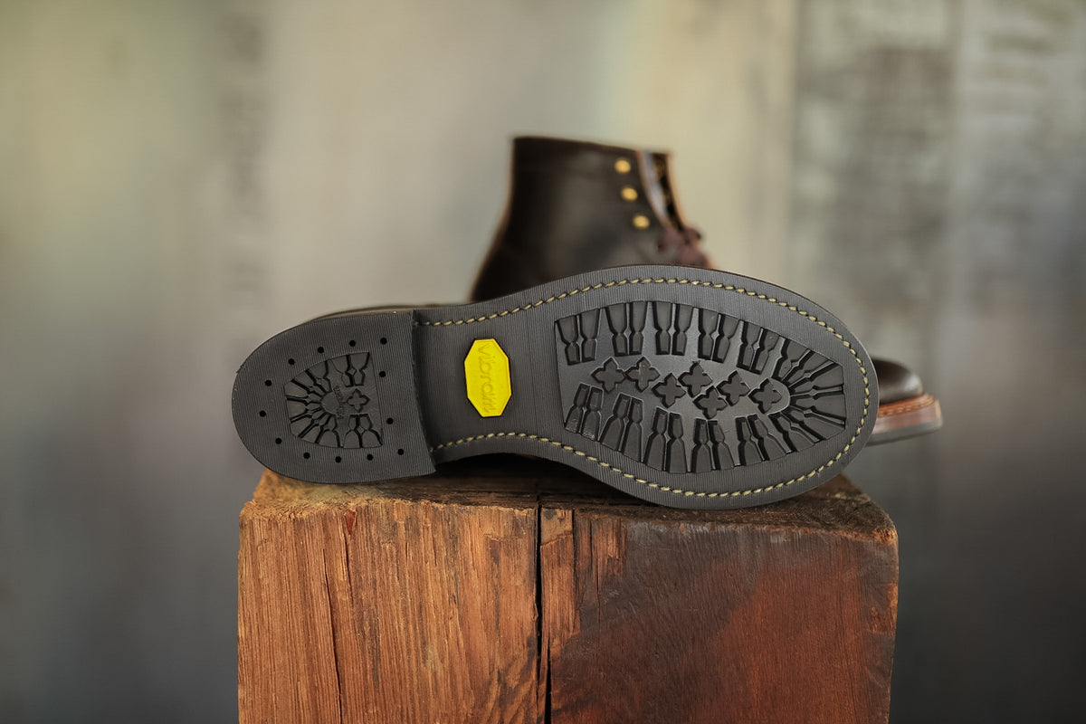 Close-up of a boot sole with tread pattern on a wooden block against a blurred background