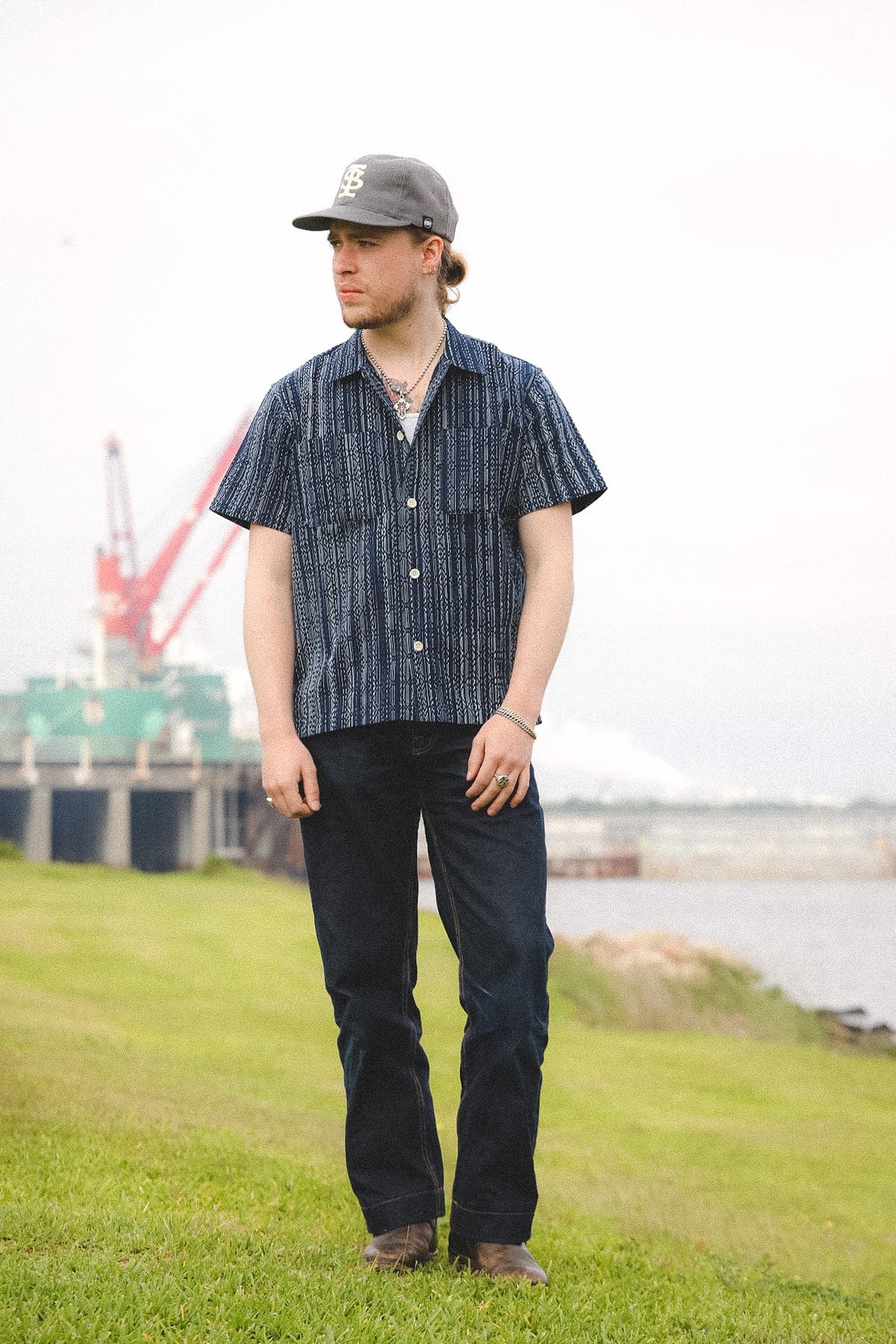 Man wearing a patterned shirt and cap standing on grass with a blurred background