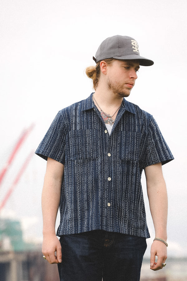 Man wearing a blue patterned shirt and gray cap outdoors