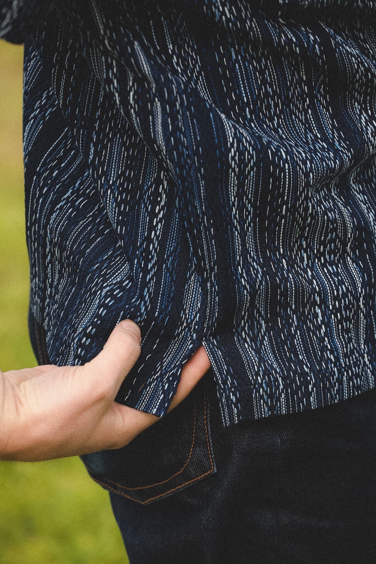 Close-up of a person wearing a dark blue patterned jacket with a blurred green background