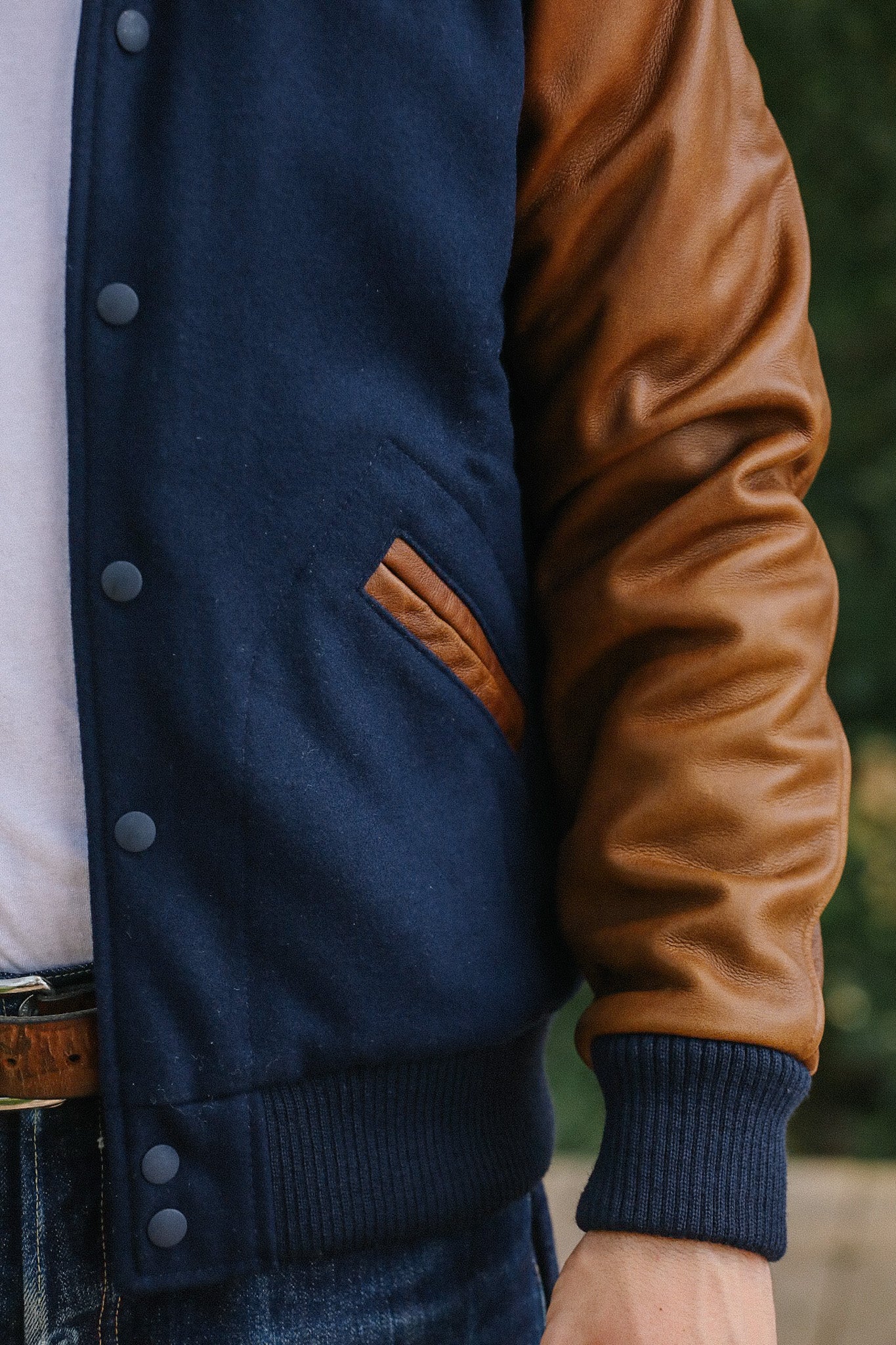 Close-up of a navy blue and brown leather sleeve varsity jacket with button closures and ribbed cuffs