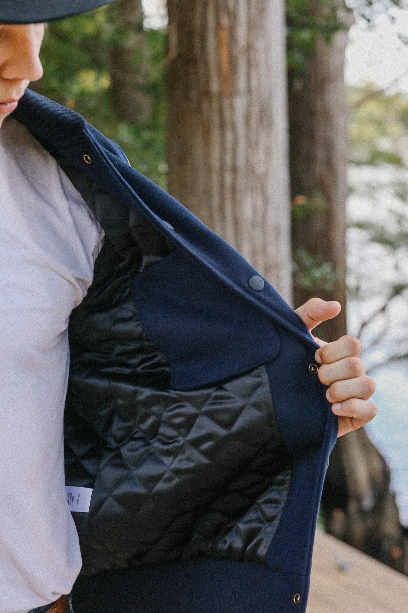 Close-up of a person wearing a navy blue quilted-lined jacket, outdoor forest background