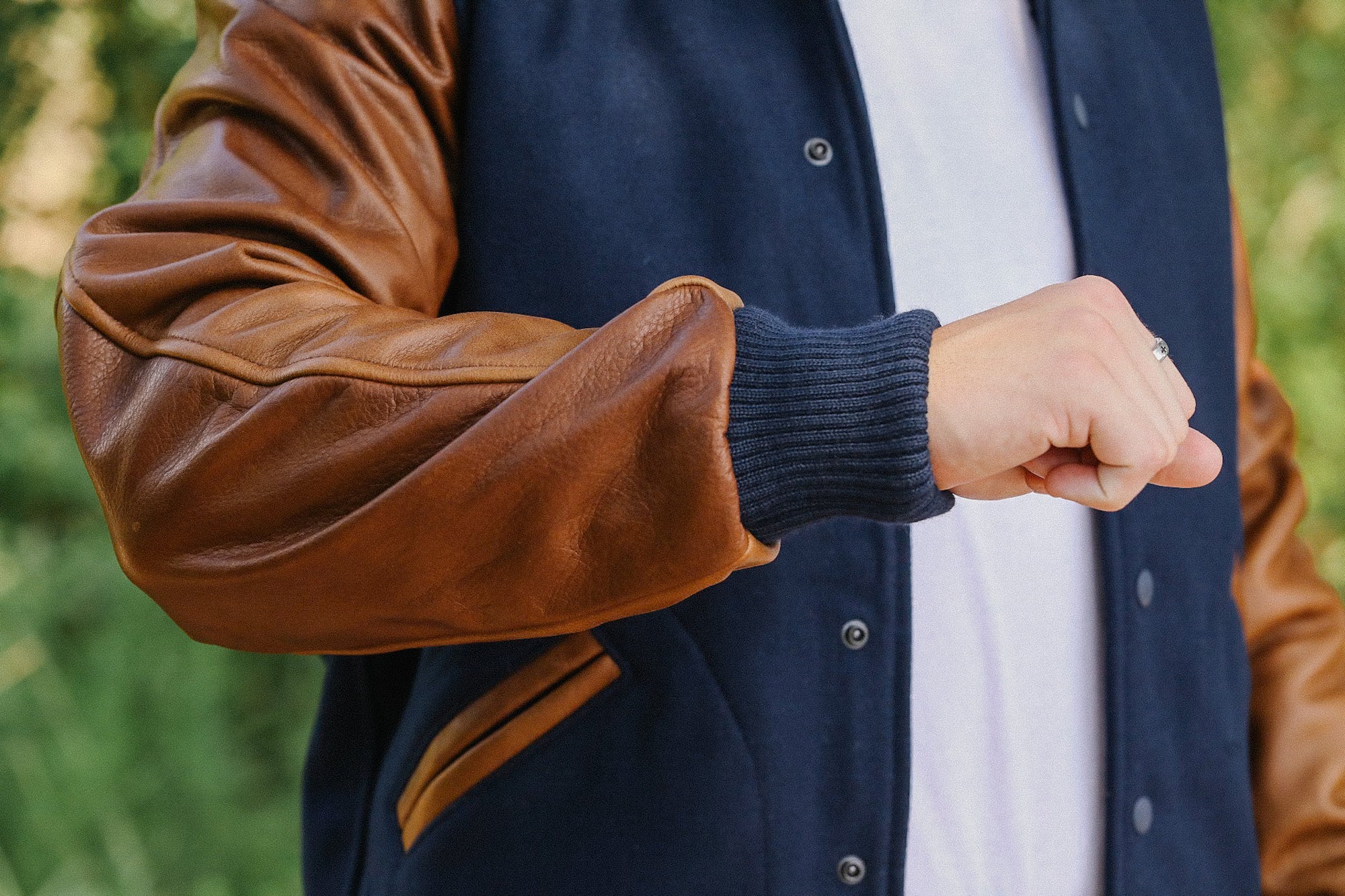 Person wearing navy blue and brown leather varsity jacket with ribbed cuffs outdoors