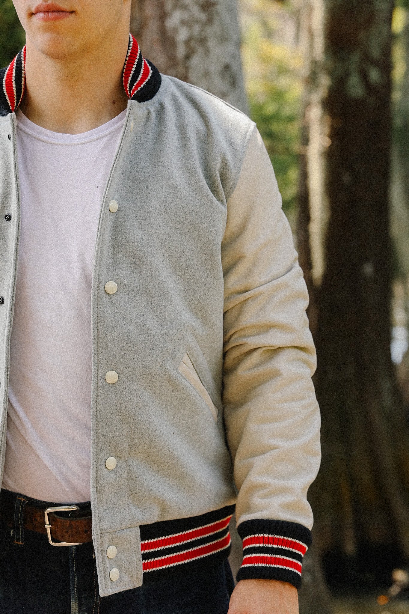 Man wearing gray varsity jacket with white sleeves and red striped collar and cuffs outdoors