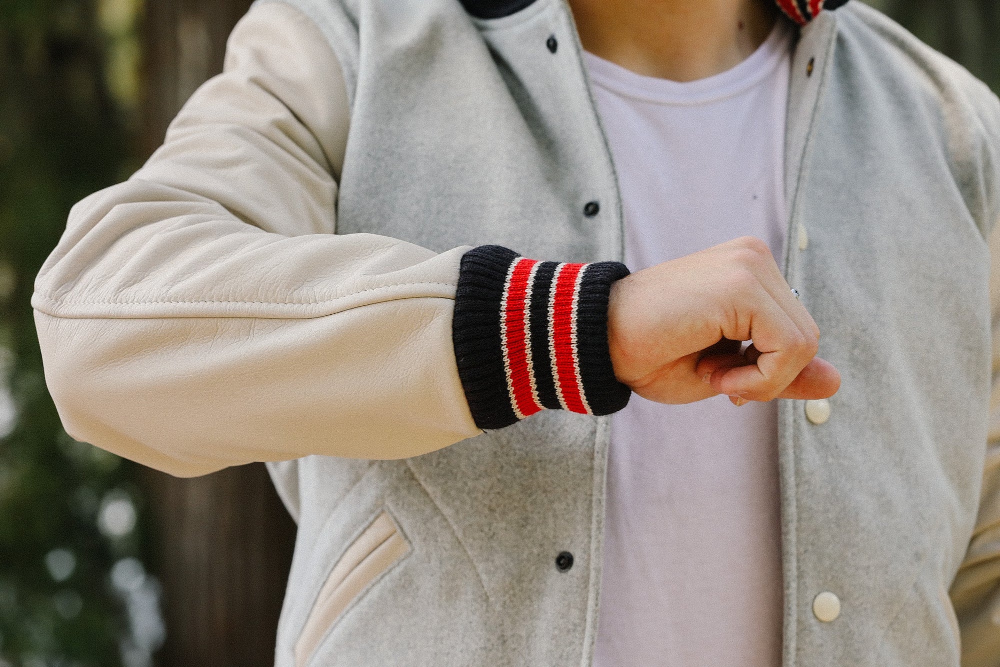 Person wearing grey and white varsity jacket with black, red, and white striped cuff over white t-shirt