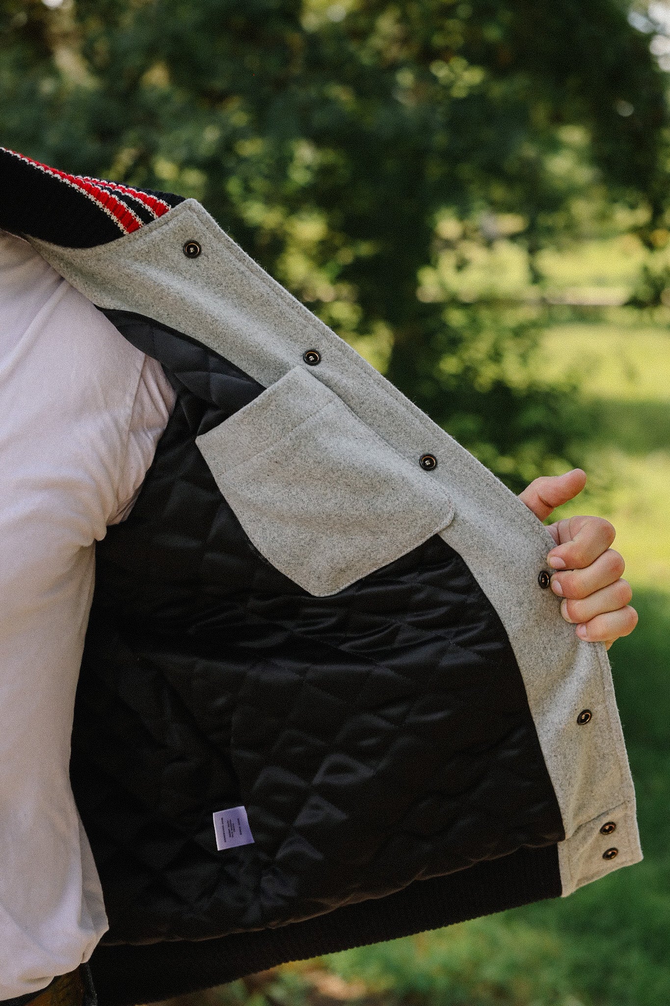 Man holding open a quilted black and grey jacket lining with interior pocket outdoors