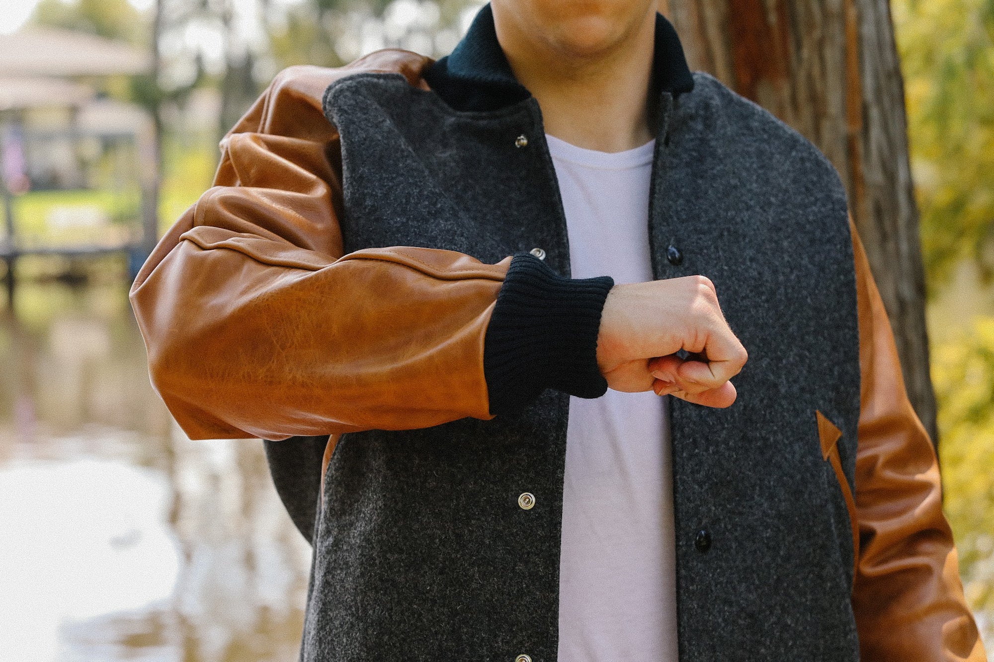 Man wearing grey wool and brown leather sleeve varsity jacket outdoors near water