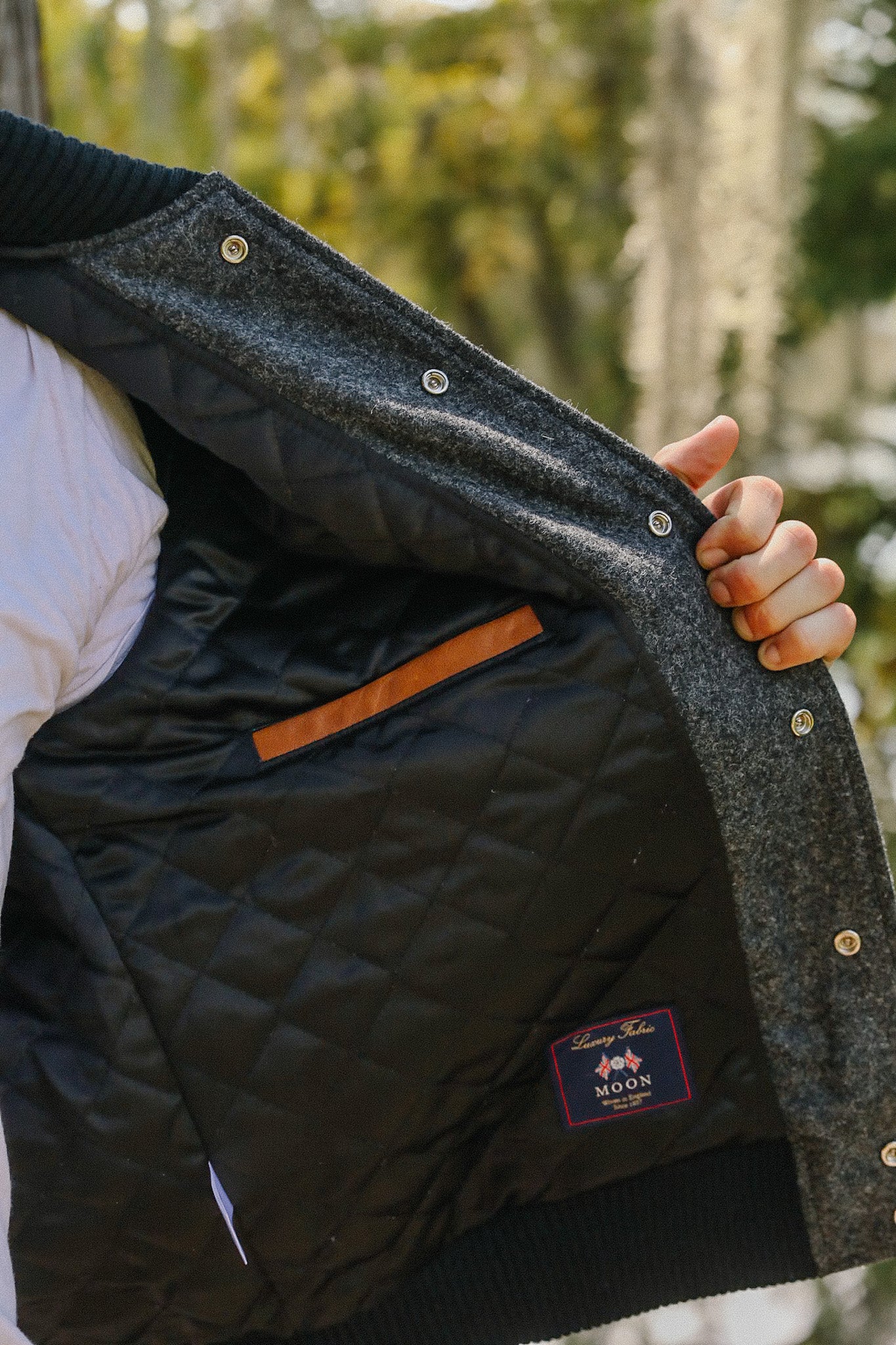 Hand holding open a gray wool jacket with black quilted lining and luxury fabric label from Moon