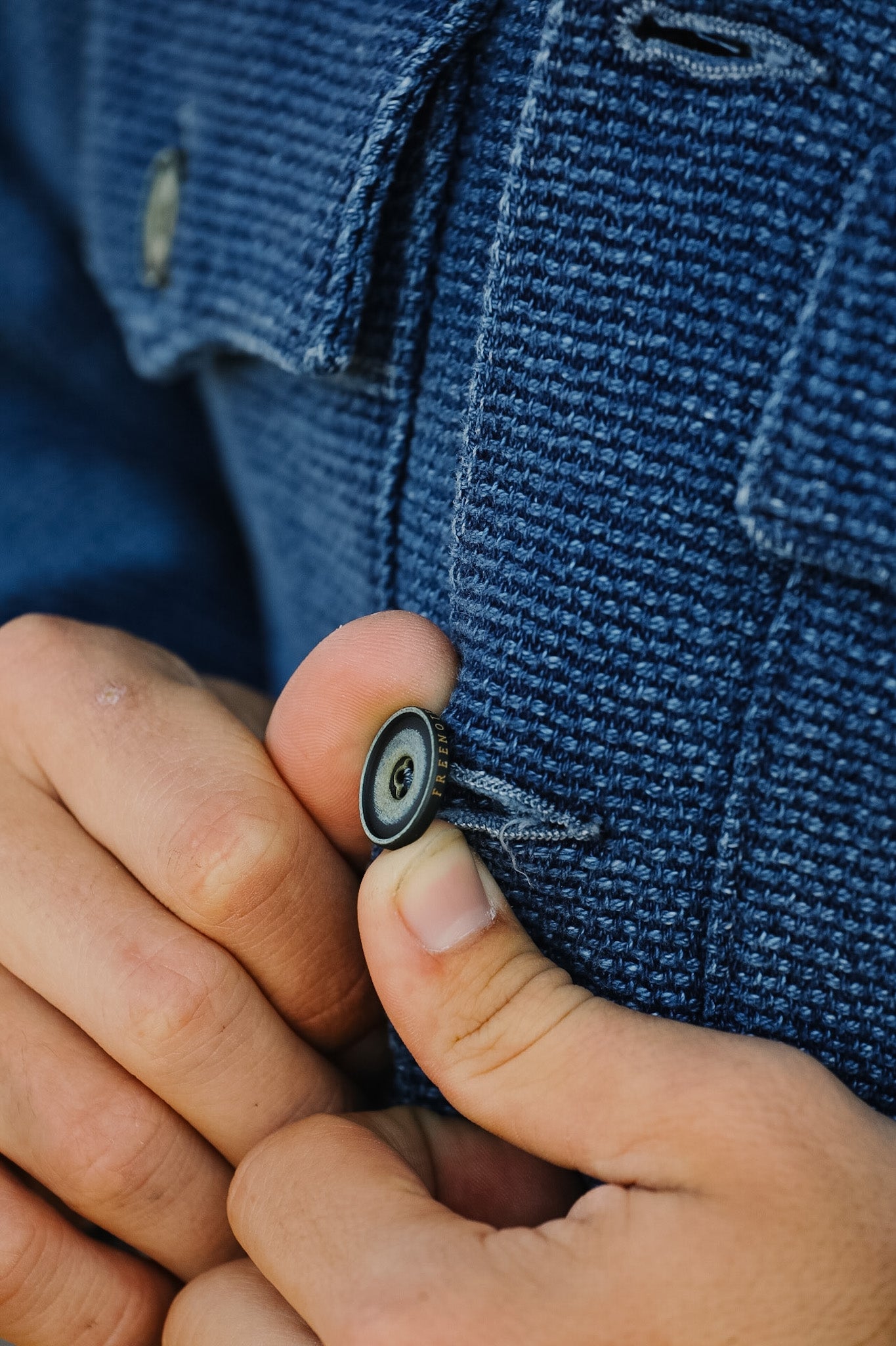 Close-up of a hand buttoning a blue textured jacket