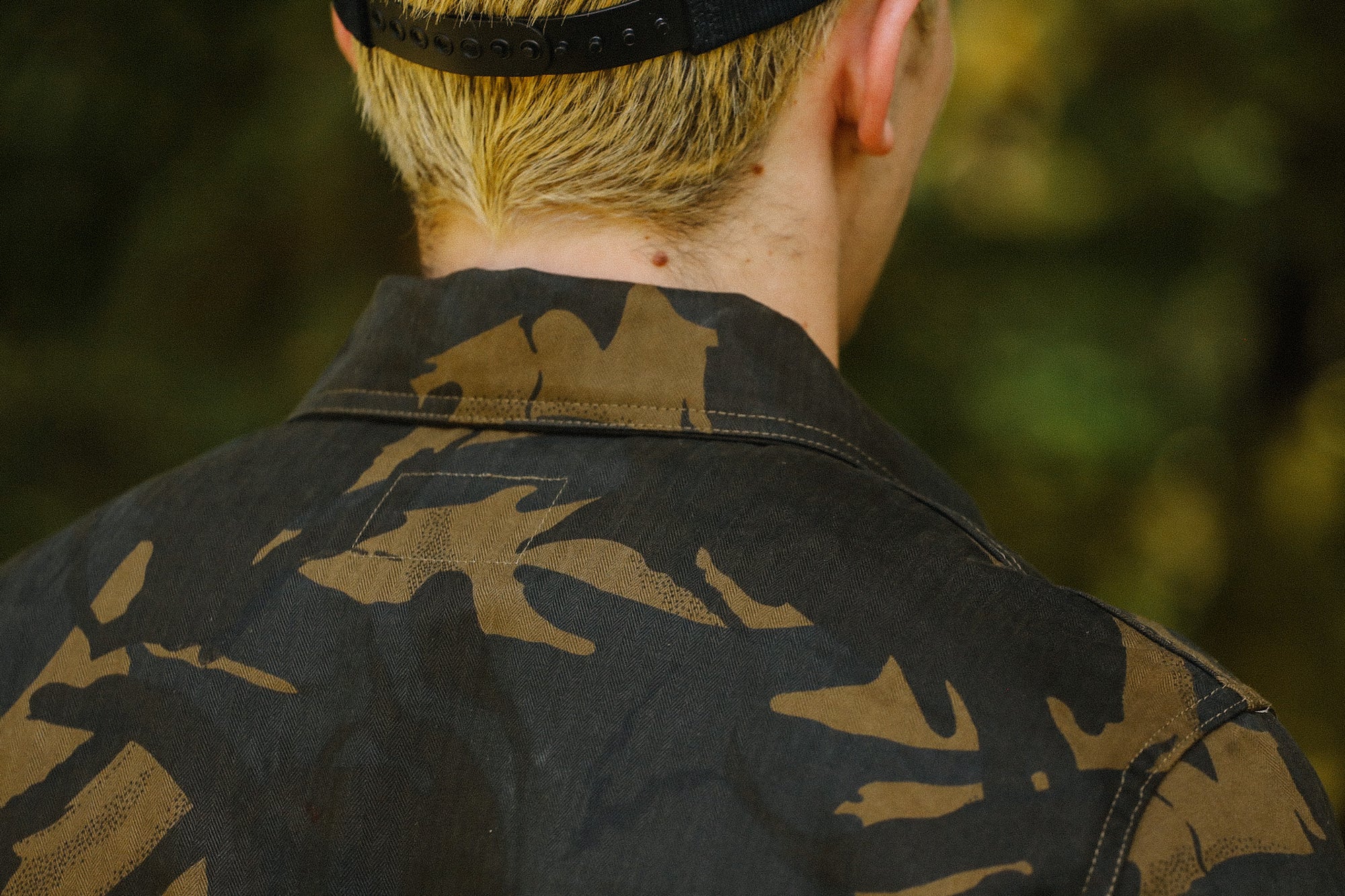 Close-up of a man wearing a black and brown camouflage jacket and black cap in outdoor setting