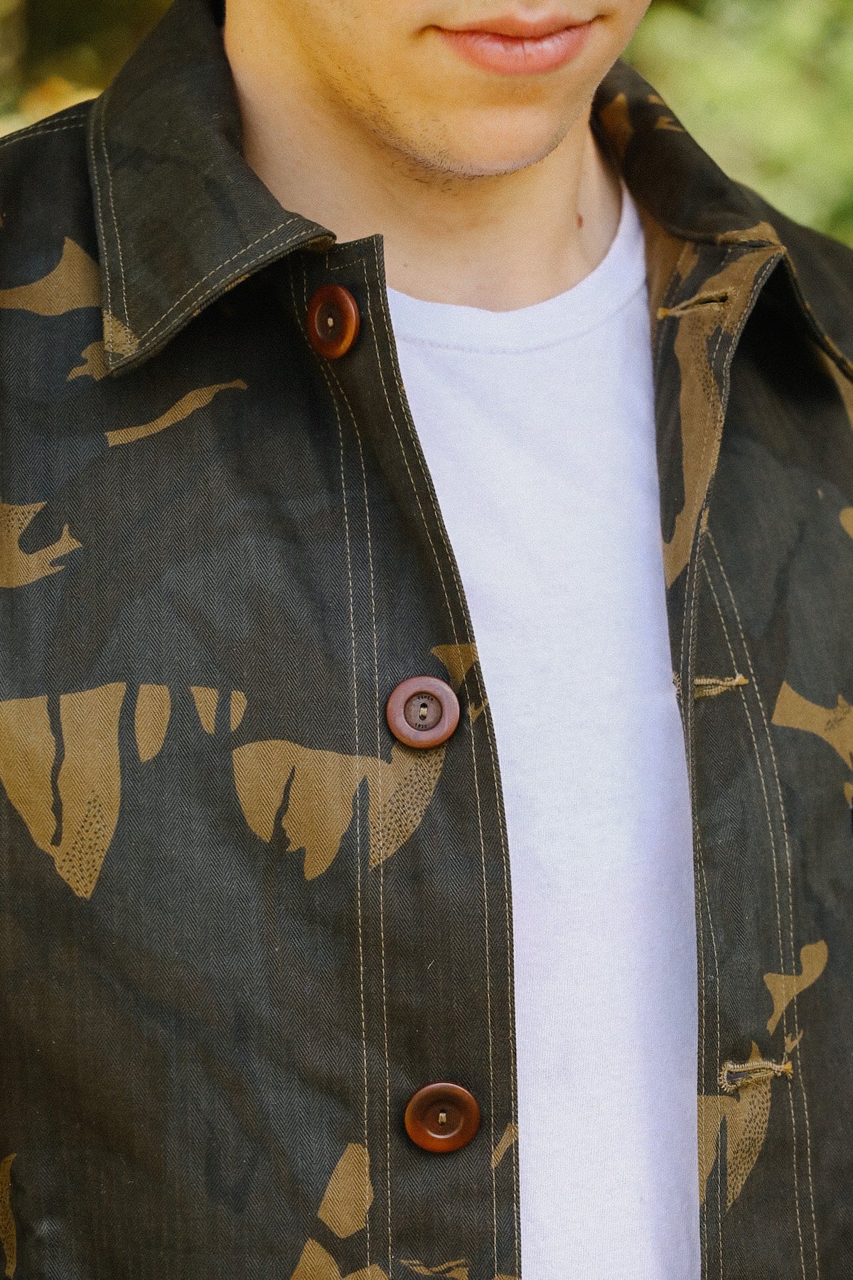 Close-up of a person wearing a camo print jacket with brown buttons over a white t-shirt