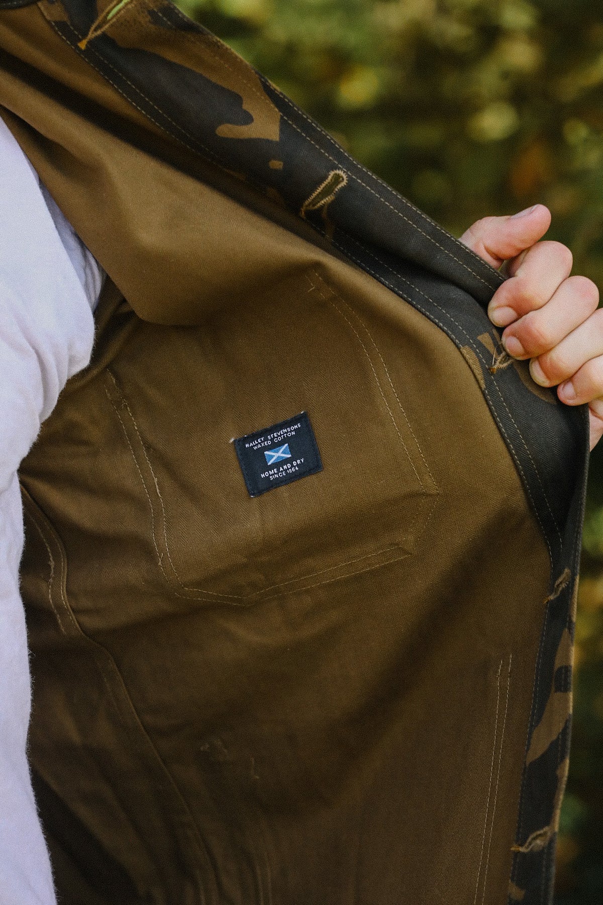 Hand holding open the inside of a brown waxed cotton jacket with Haley Stevenson's label