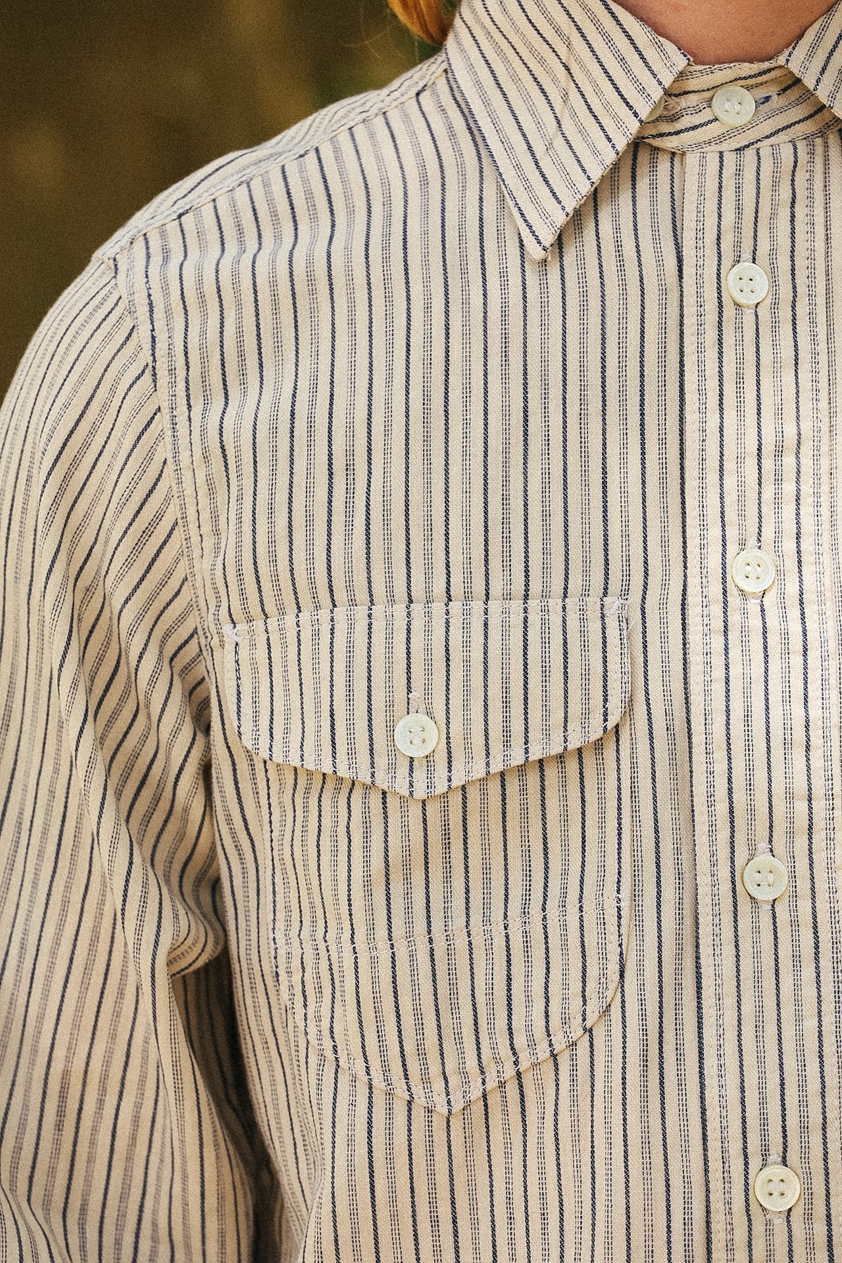 Close-up of a person wearing a long-sleeve button-up shirt with vertical navy and beige stripes, featuring a chest pocket and white buttons.