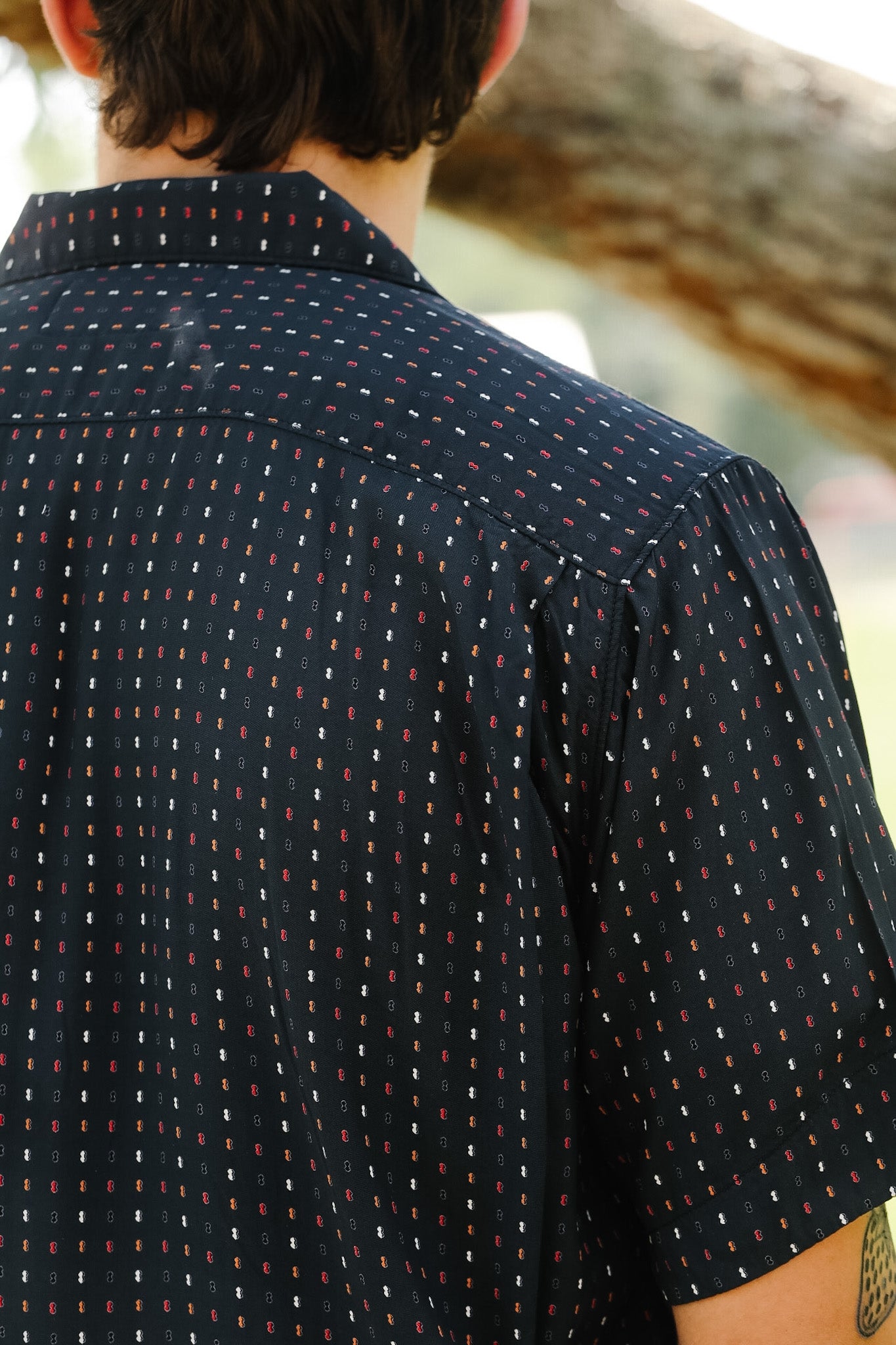 Person wearing a dark patterned shirt with a blurred natural background